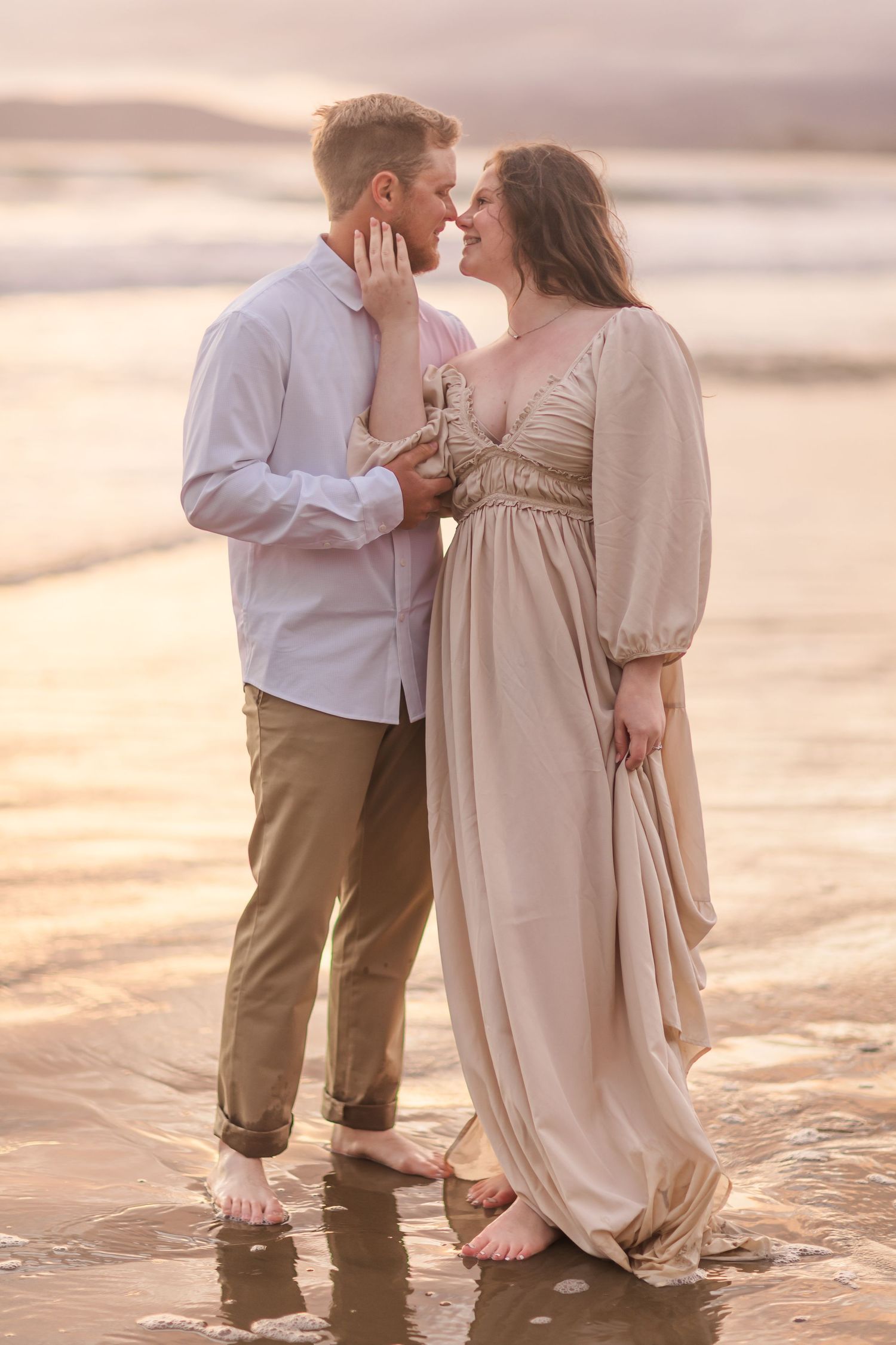 A romantic sunset moment shared between a couple standing in shallow beach water.
