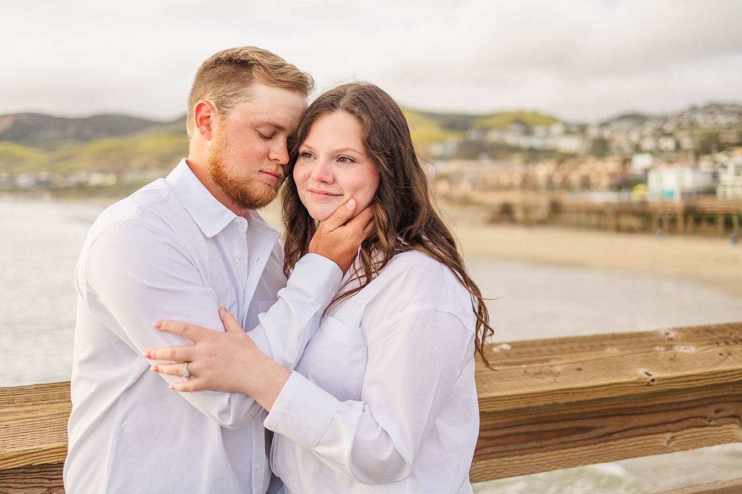 A tender moment between a couple in matching white shirts on a coastal boardwalk at sunset.