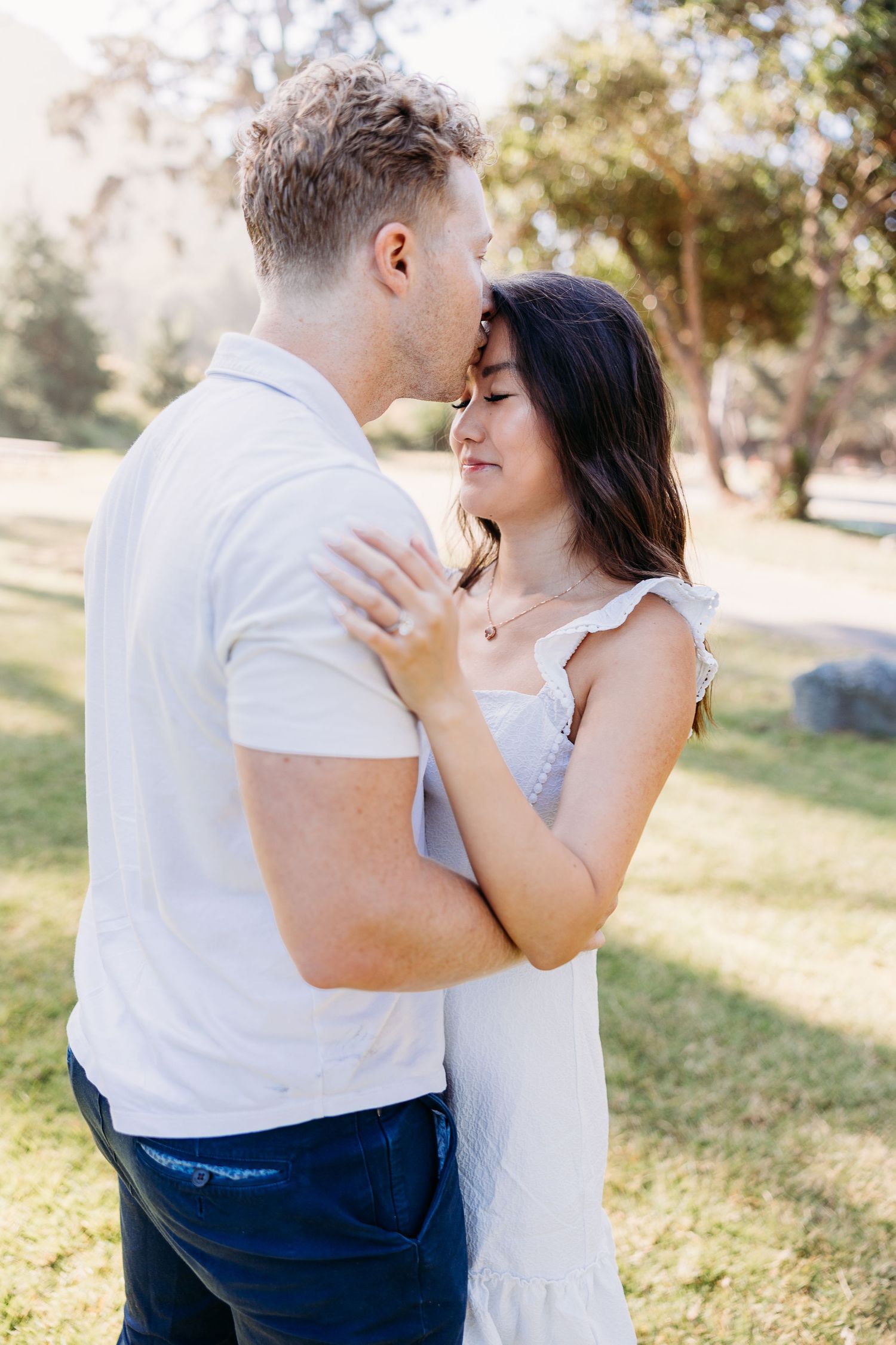 Couple in white and navy outfits share tender embrace in sunny park.