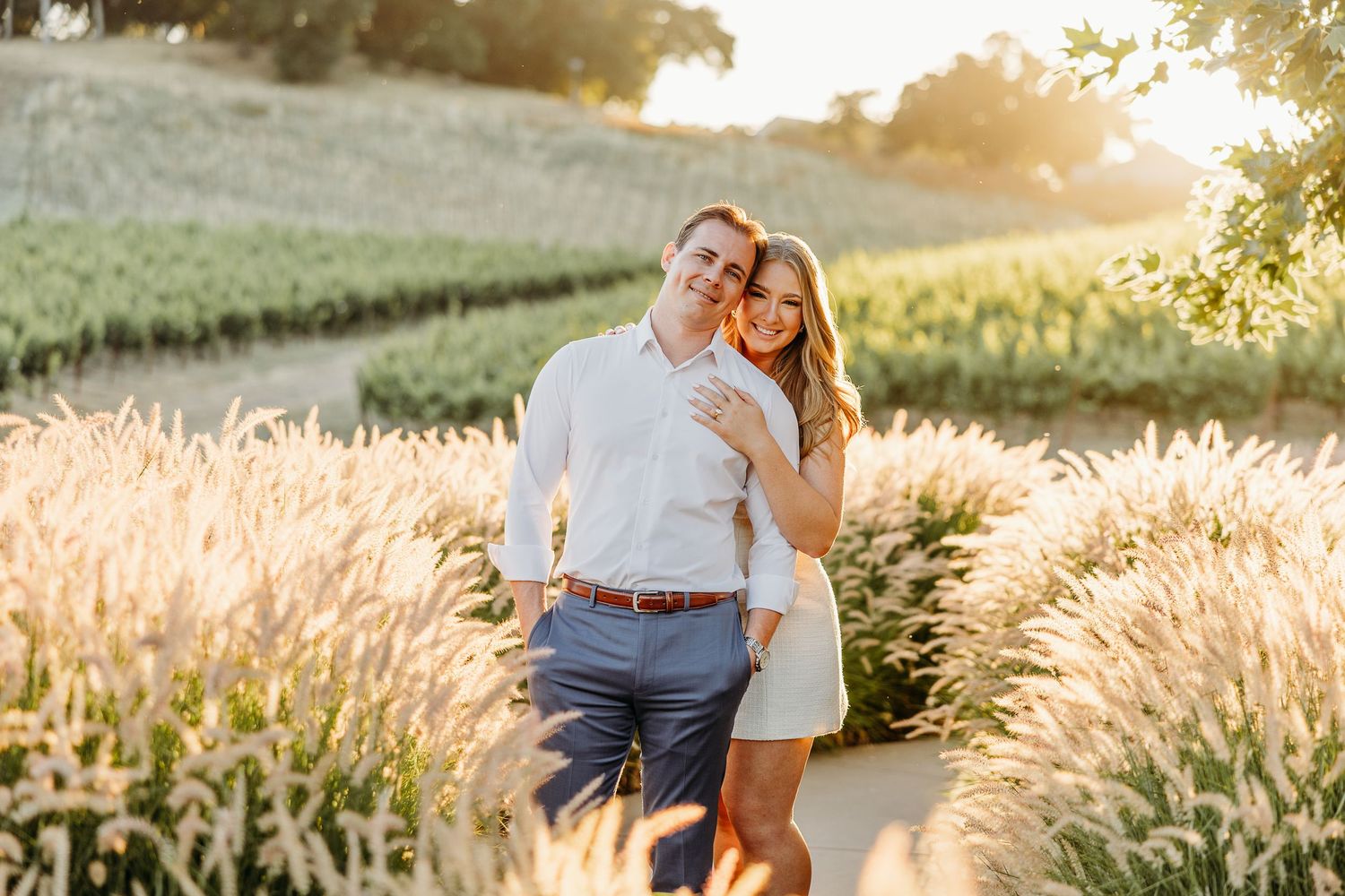 A romantic couple embraces outside a rustic doorway with stone walls and wine barrel decoration.