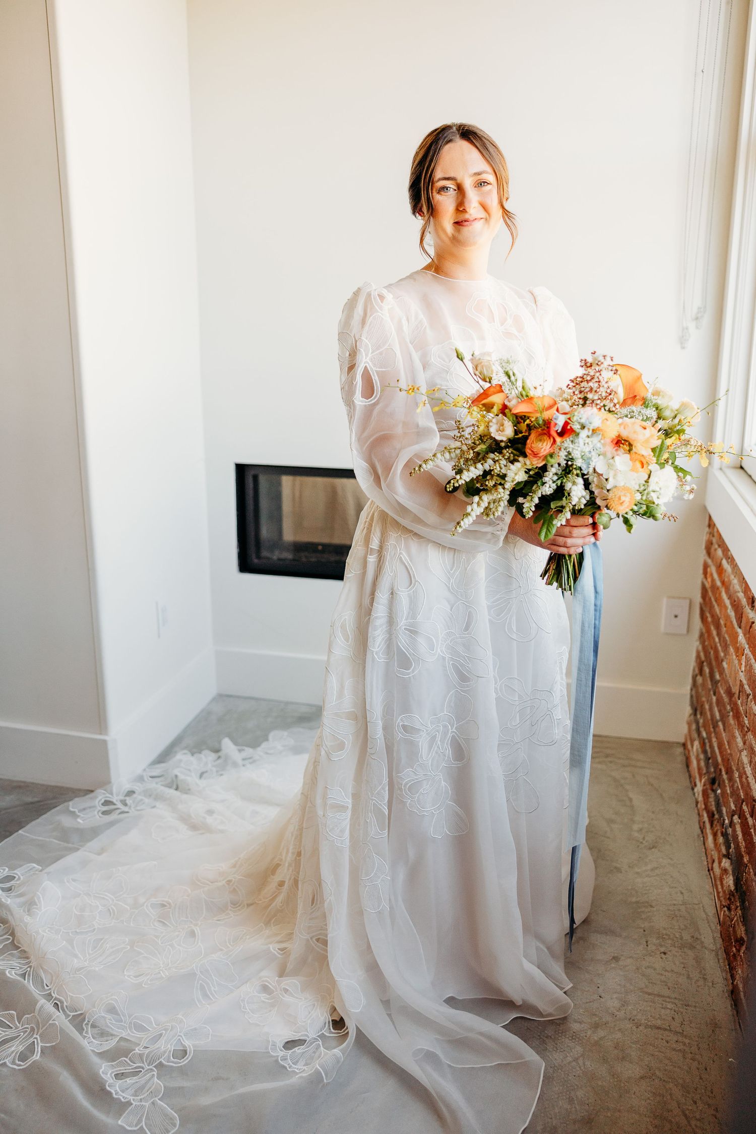 Someone wearing a flowing white wedding gown holds a colorful bouquet against a brick wall backdrop at Hotel Cerro SLO..