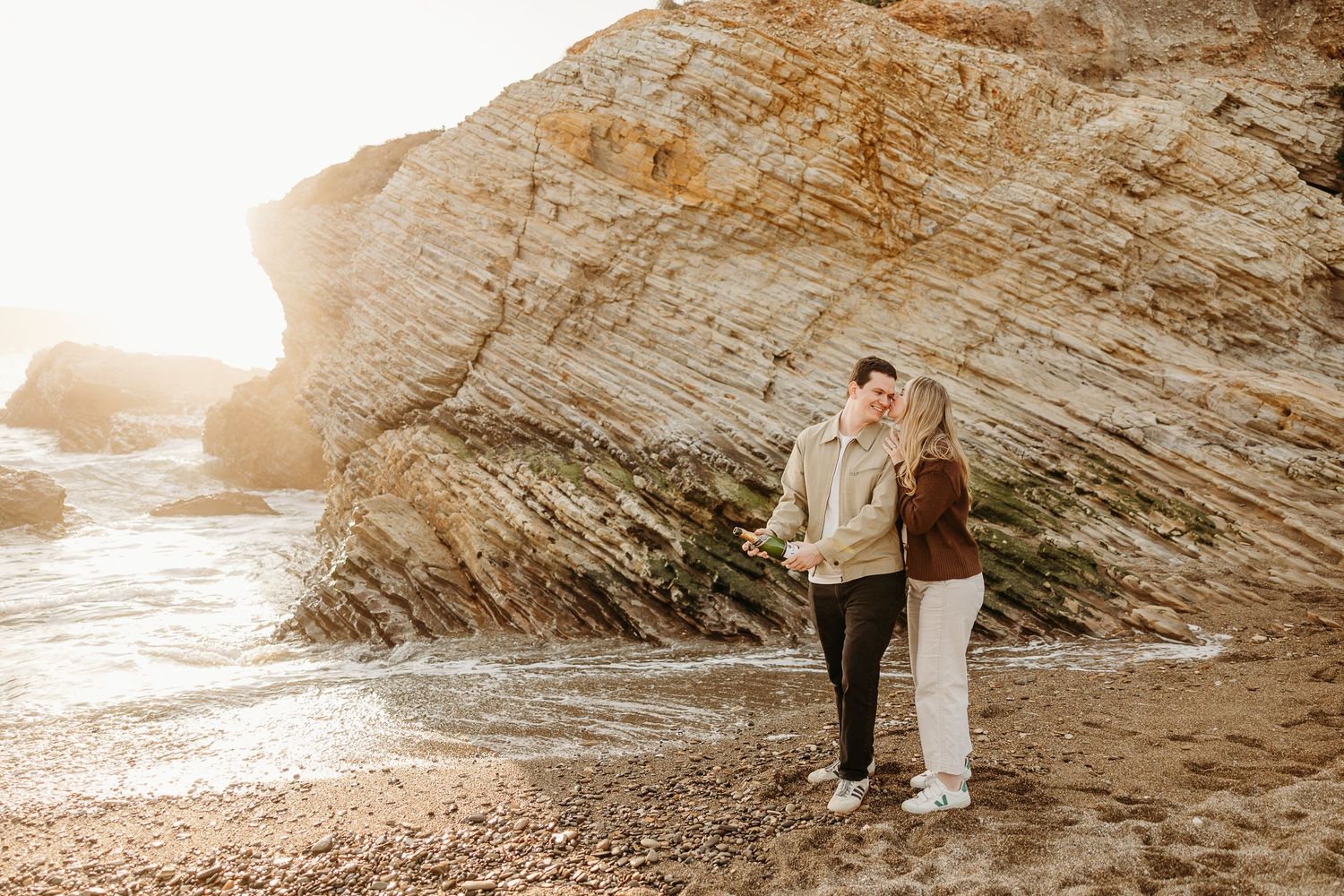 Rocky beach landscape with dramatic cliffs and ocean waves during golden hour.