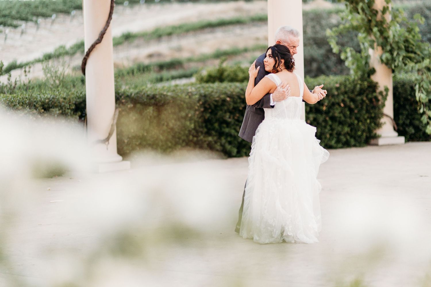 A romantic embrace on an outdoor patio surrounded by vineyard scenery.