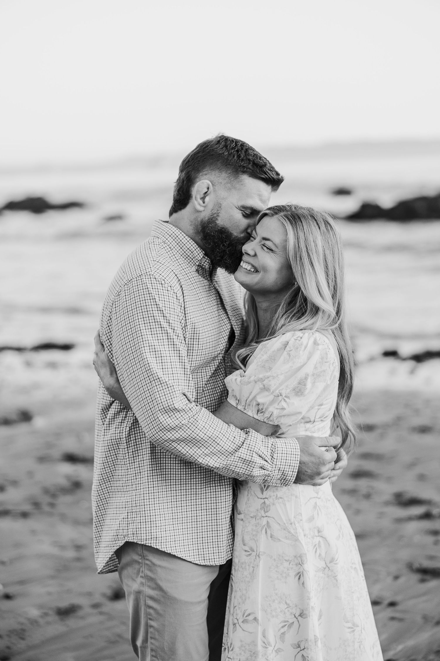 Intimate black and white portrait session of couple embracing on sandy beach.