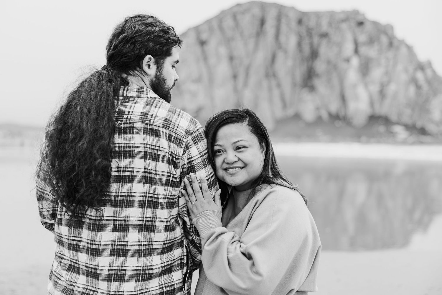 A couple laughs together while spending time at Morro Rock State Beach in California on an overcast day.