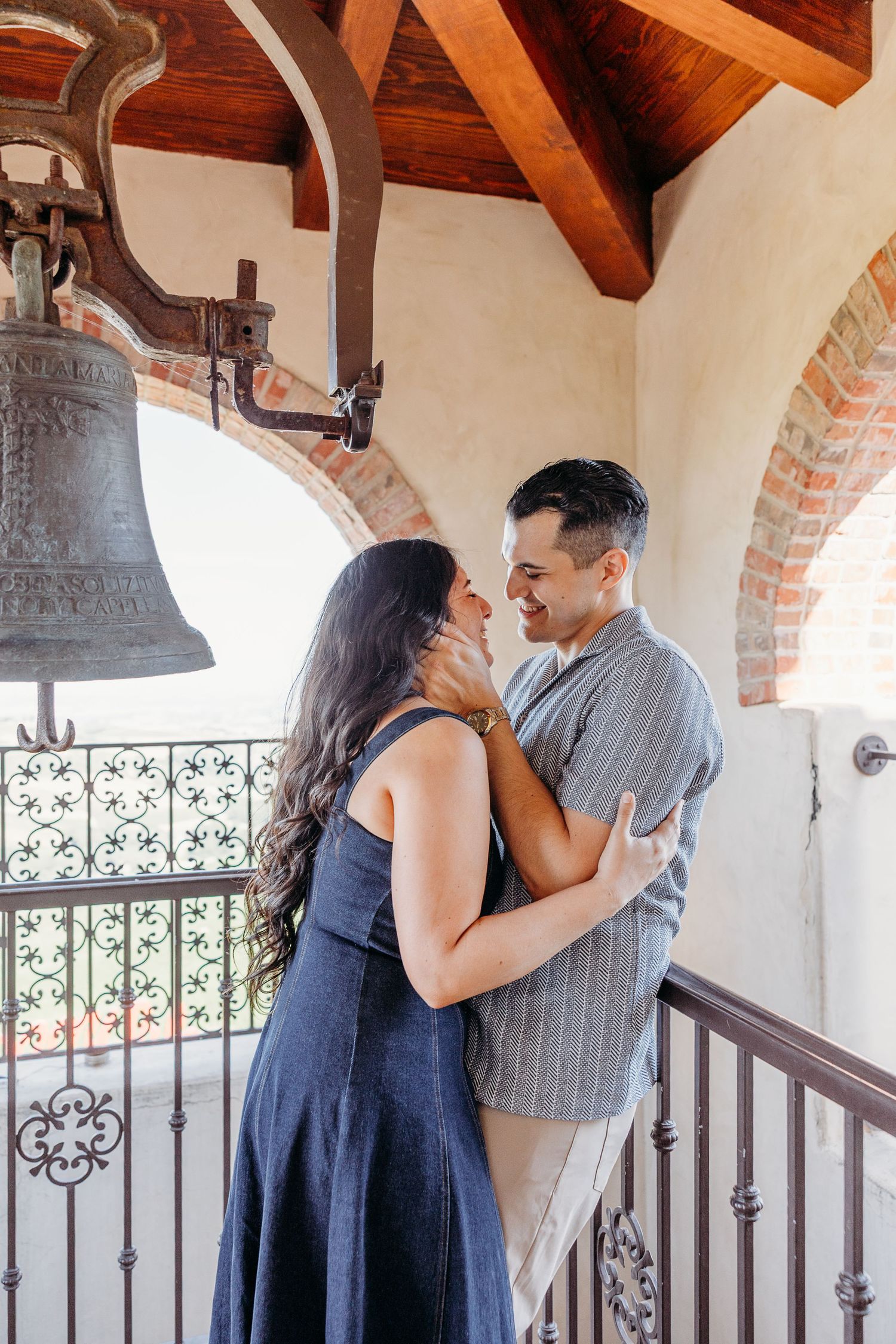 Romantic couple embracing by an antique bell in an architectural archway.