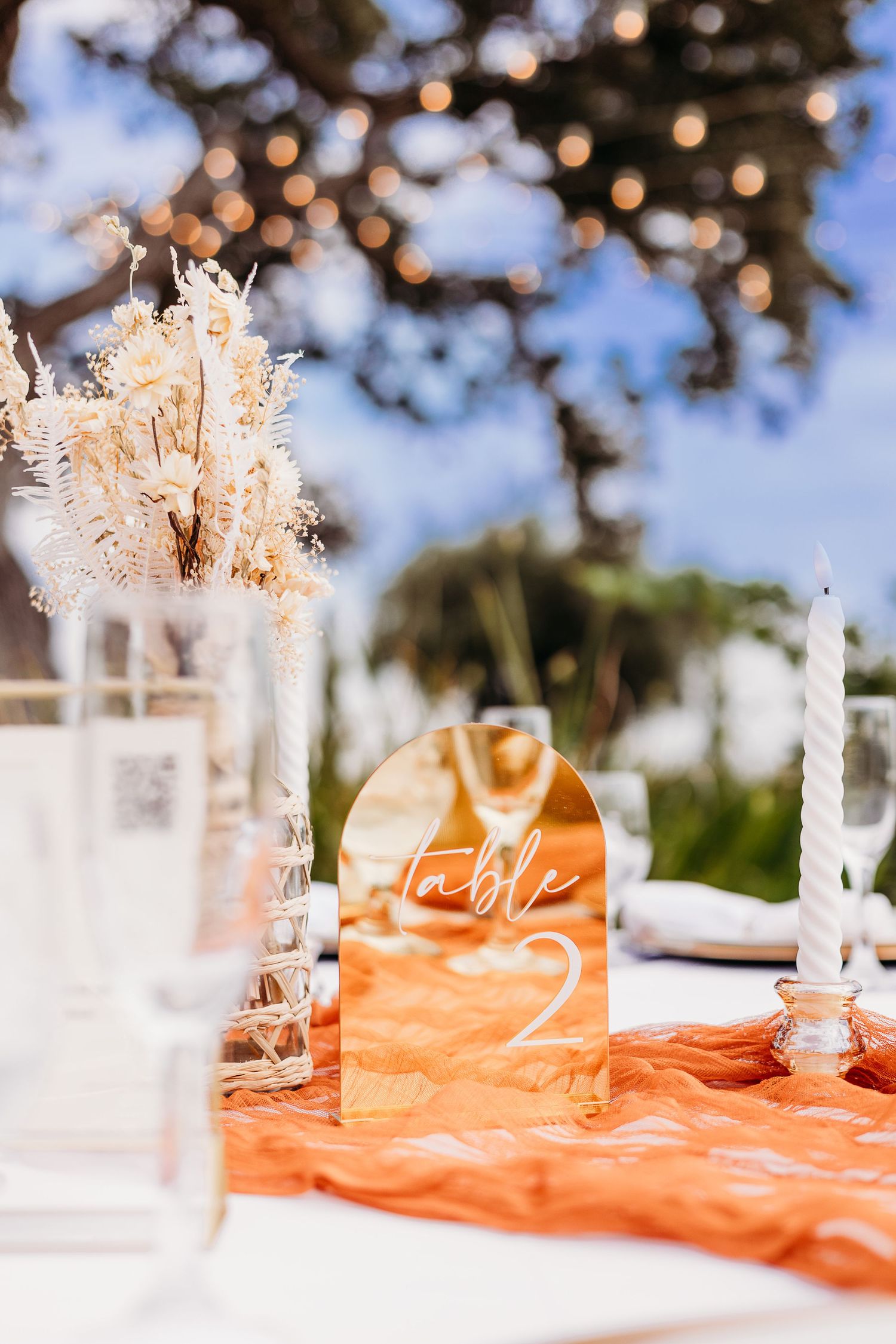 Wedding table decor featuring dried flowers, orange runners and acrylic table numbers.