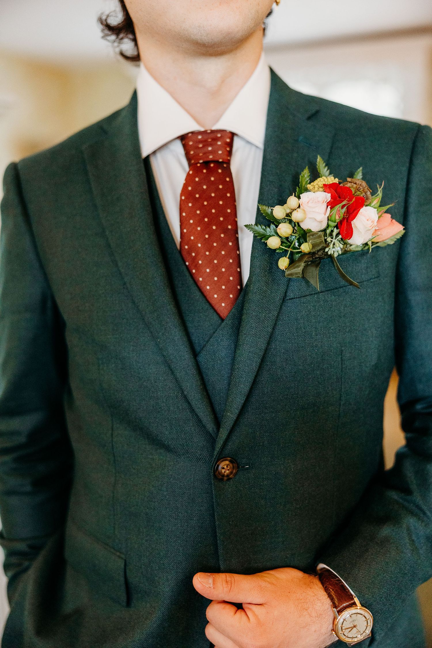 Details of a dark green wedding suit with polka dot tie and floral boutonniere.