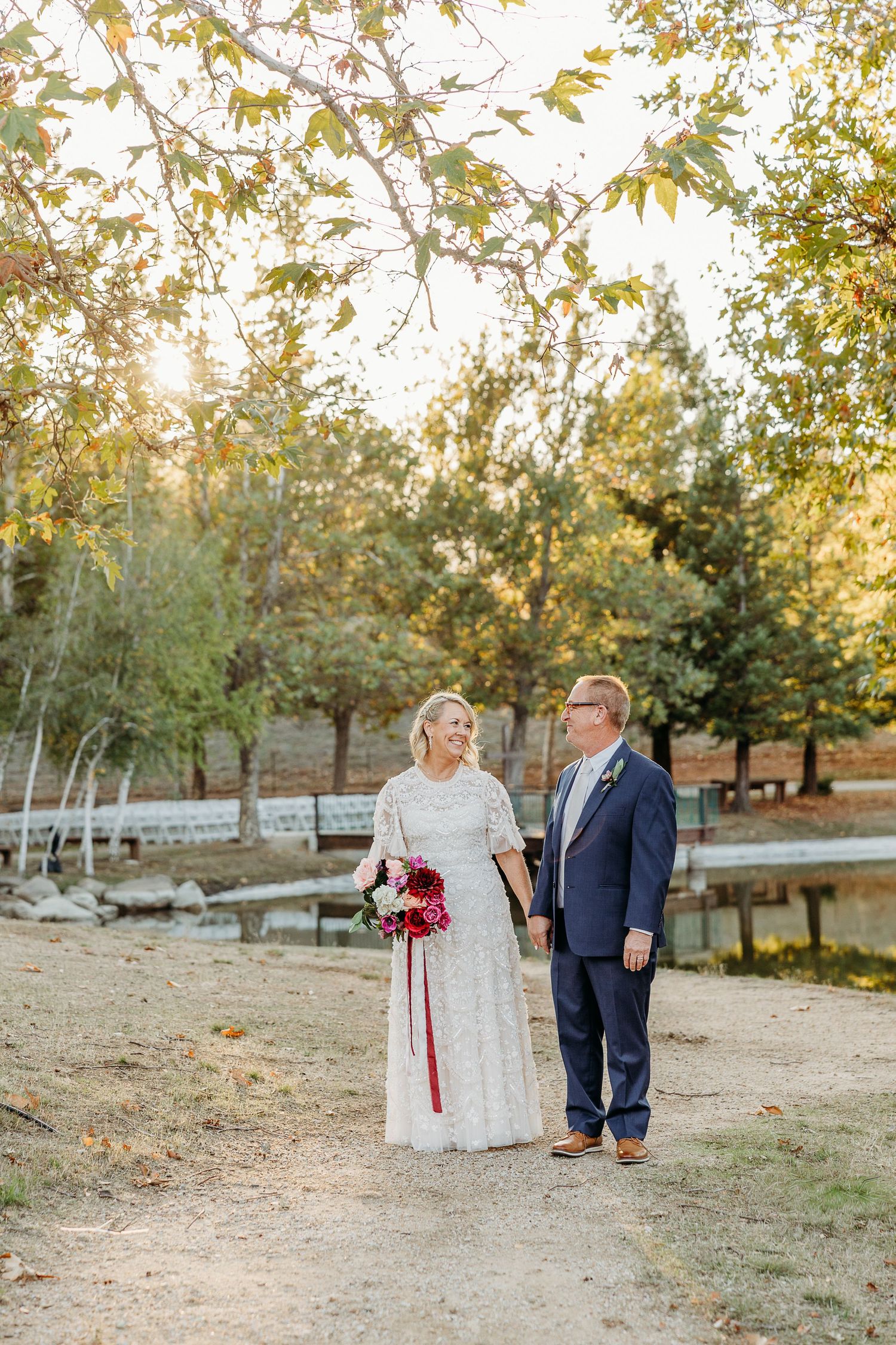 Wedding couple takes romantic photos on a rustic path surrounded by fall trees.