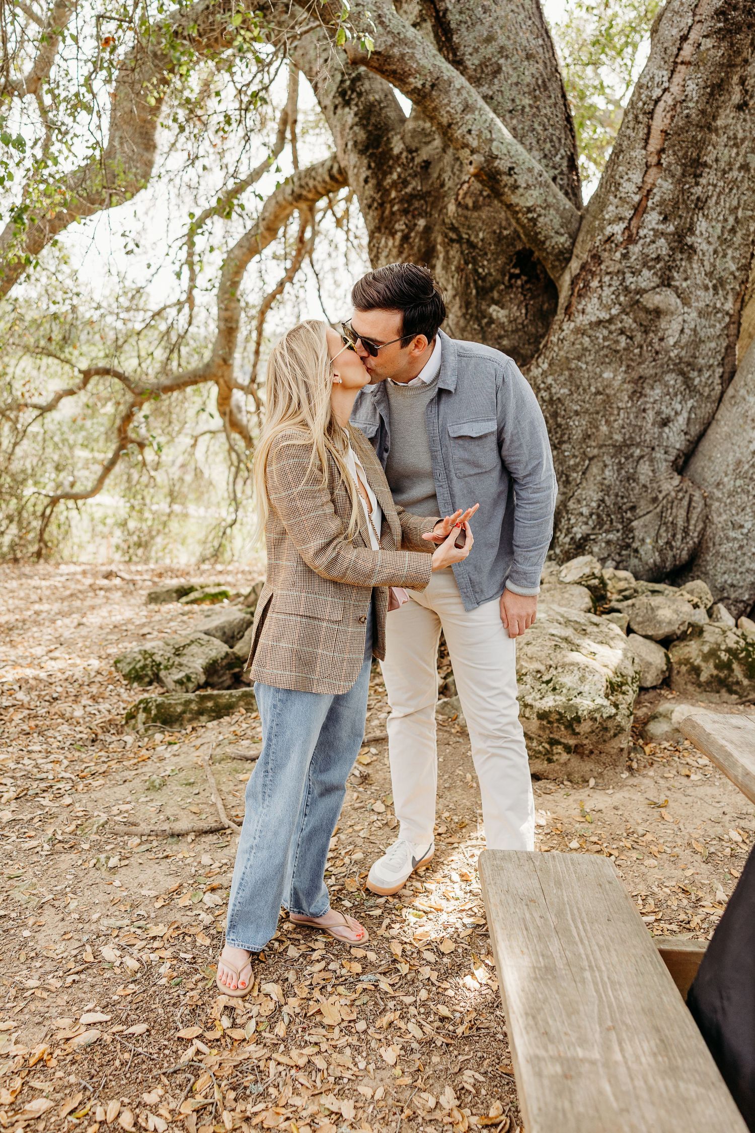A romantic moment shared between a couple under a large tree in a rustic outdoor setting.