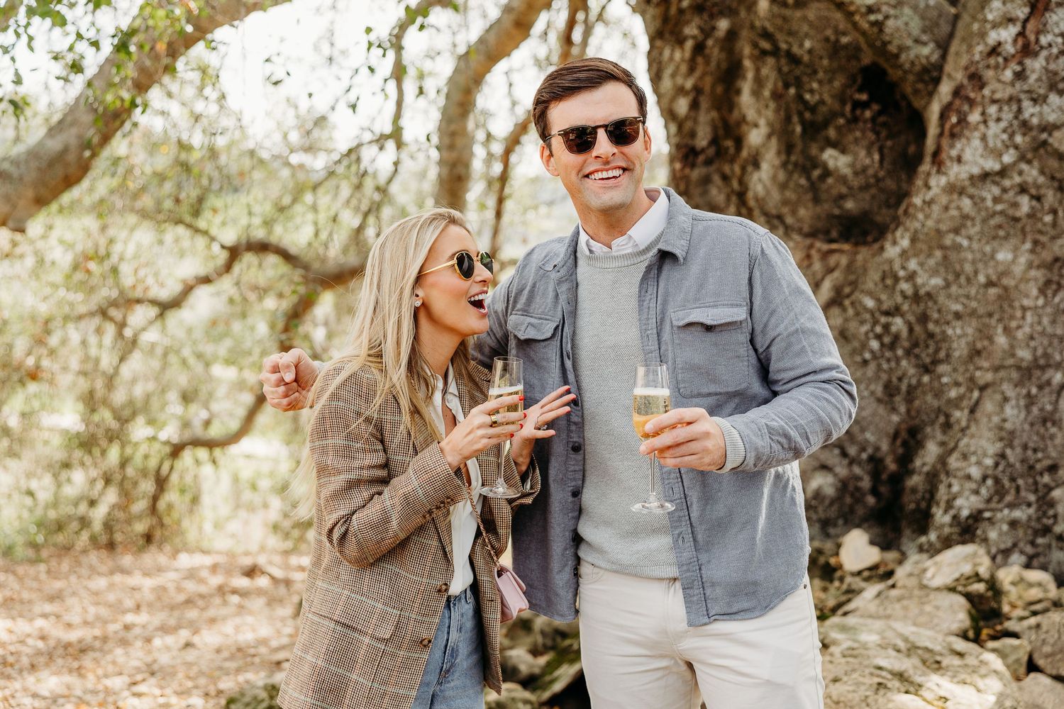 Couple enjoying wine and laughter together outdoors on a sunny day.