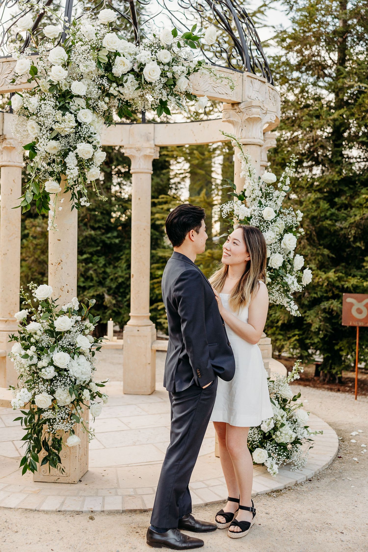 Couple sharing romantic moments under a white pergola adorned with white flowers.
