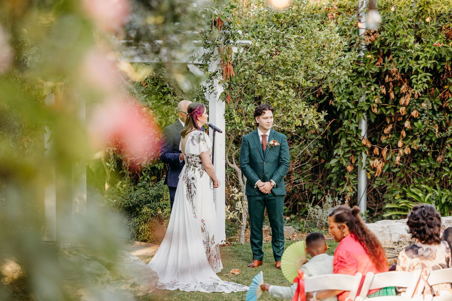 Wedding party members hugging and celebrating outdoors in a garden setting.