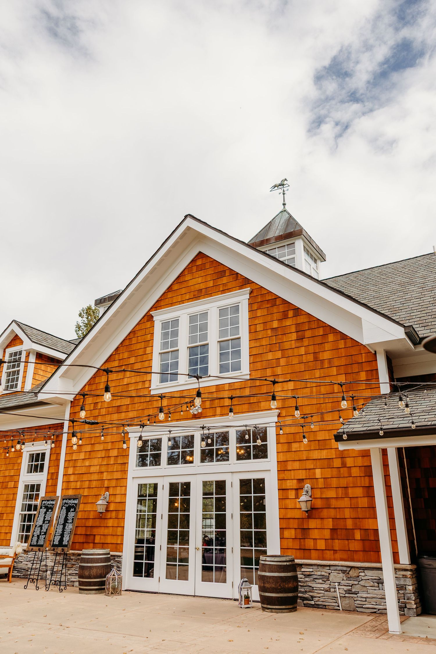 Cedar-shingled wedding venue exterior with white trim and multiple gabled rooflines against cloudy sky.