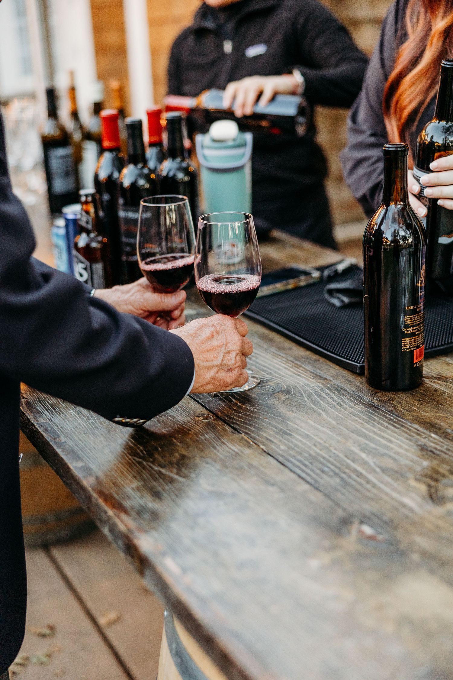 Wine bottles and glasses arranged on weathered wooden bar surface during event service.
