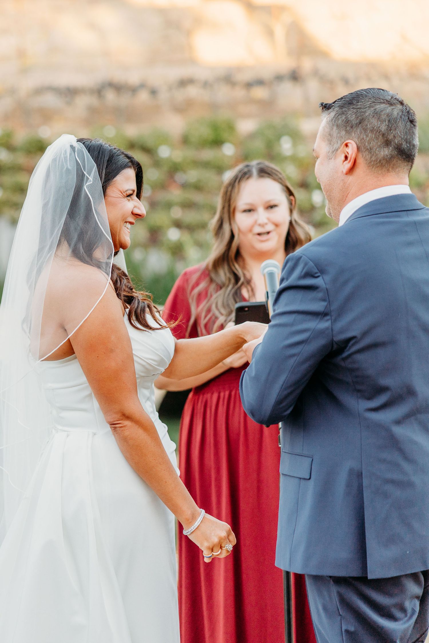 A joyful wedding ceremony moment with a bride in white dress and bridesmaids in burgundy gowns outdoors.