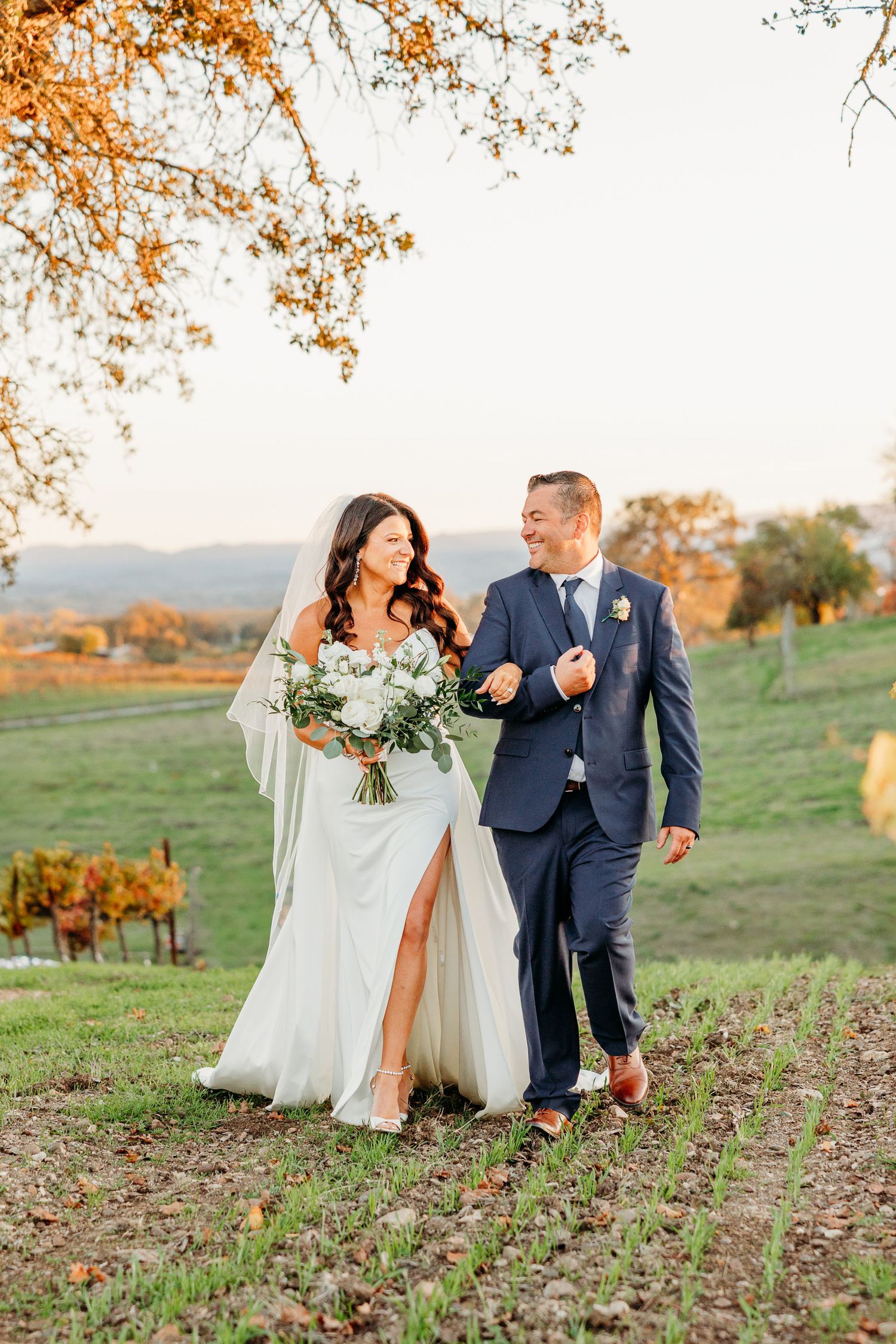 A couple walks and laughs together in an autumn field during their wedding.