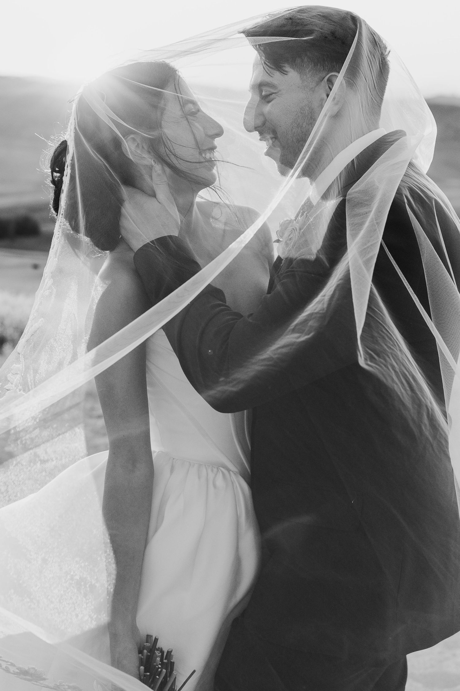 Artistic black and white wedding portraits with flowing veil creating romantic silhouettes.