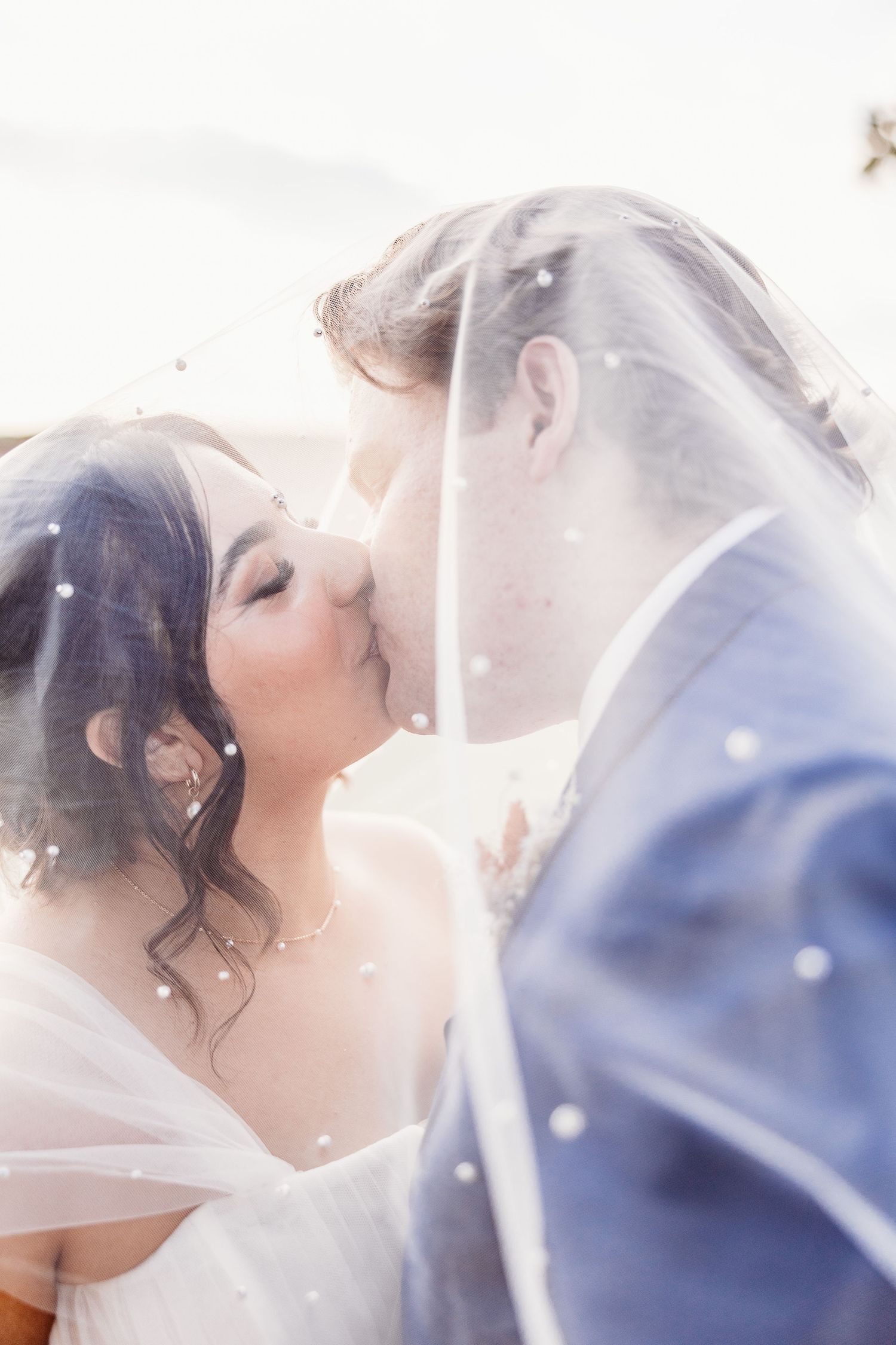 Intimate kiss between newlyweds captured through sheer wedding veil.