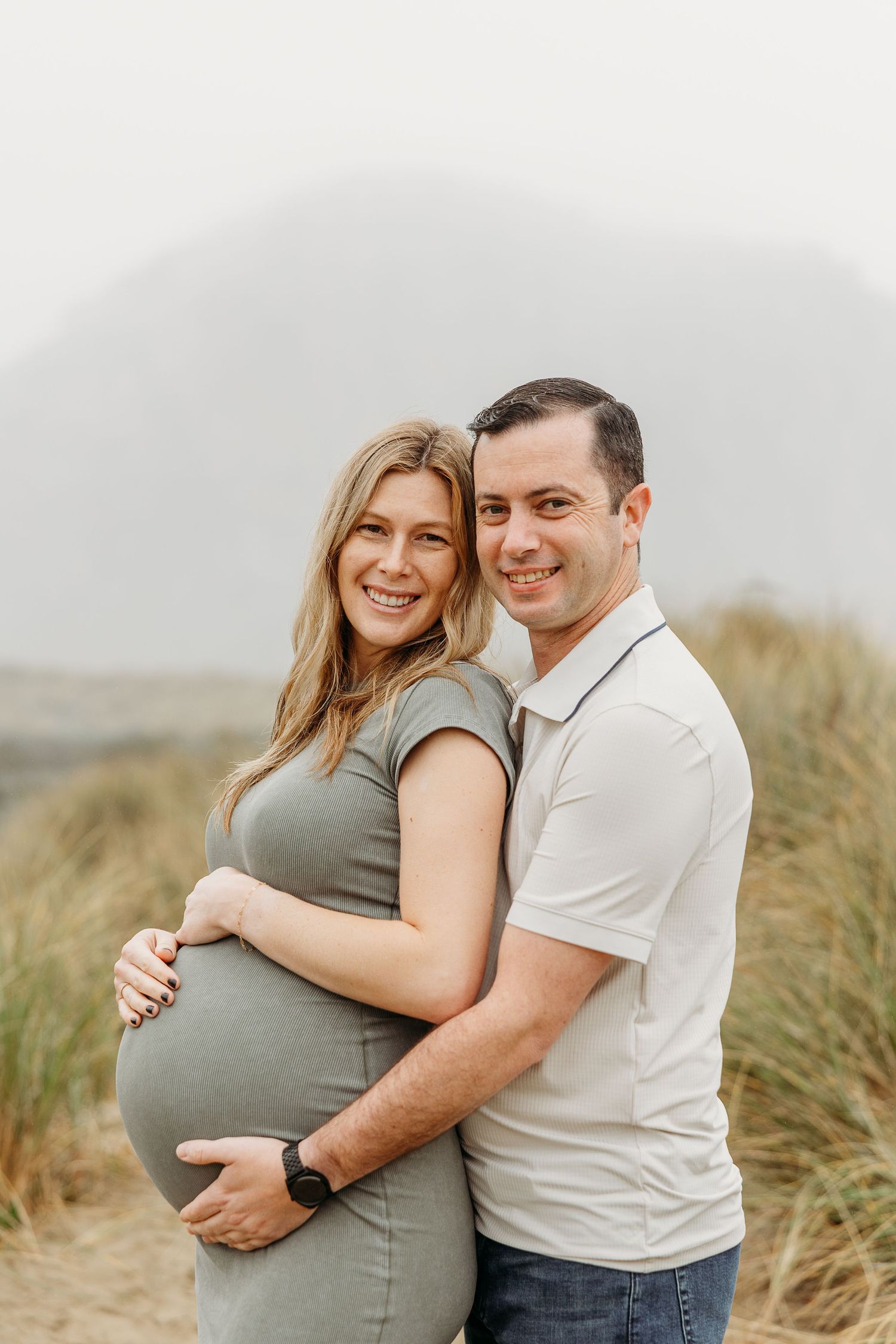 Happy couple embracing outdoors during a maternity photoshoot in nature.