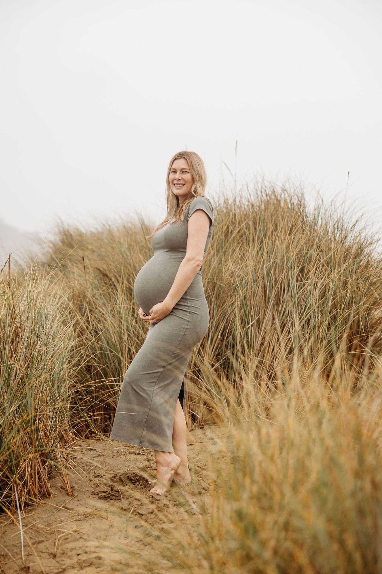 Outdoor maternity portrait featuring grey dress against natural grass landscape.