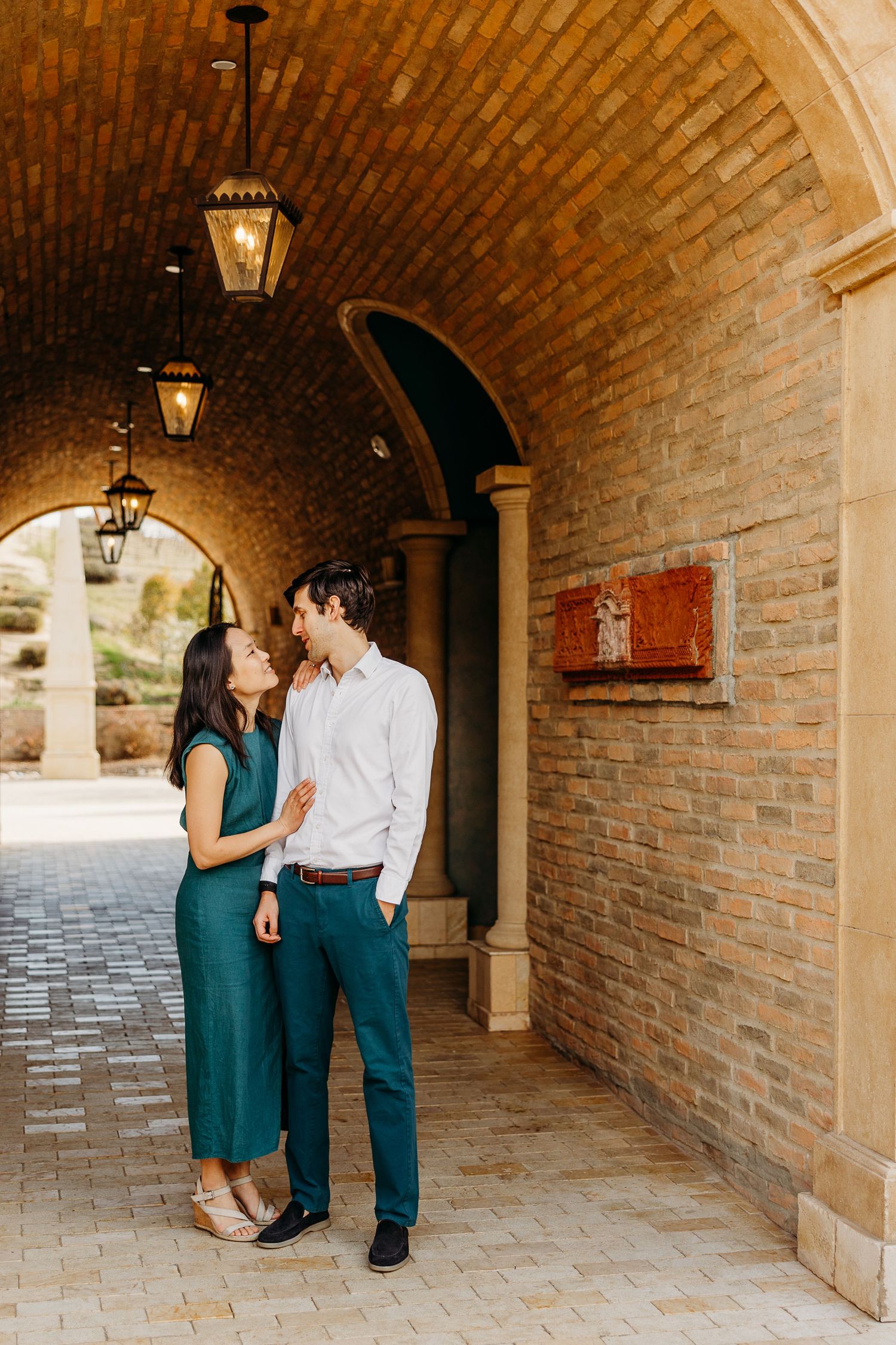 Romantic couple shares tender moments in a brick-lined archway corridor with hanging lanterns.