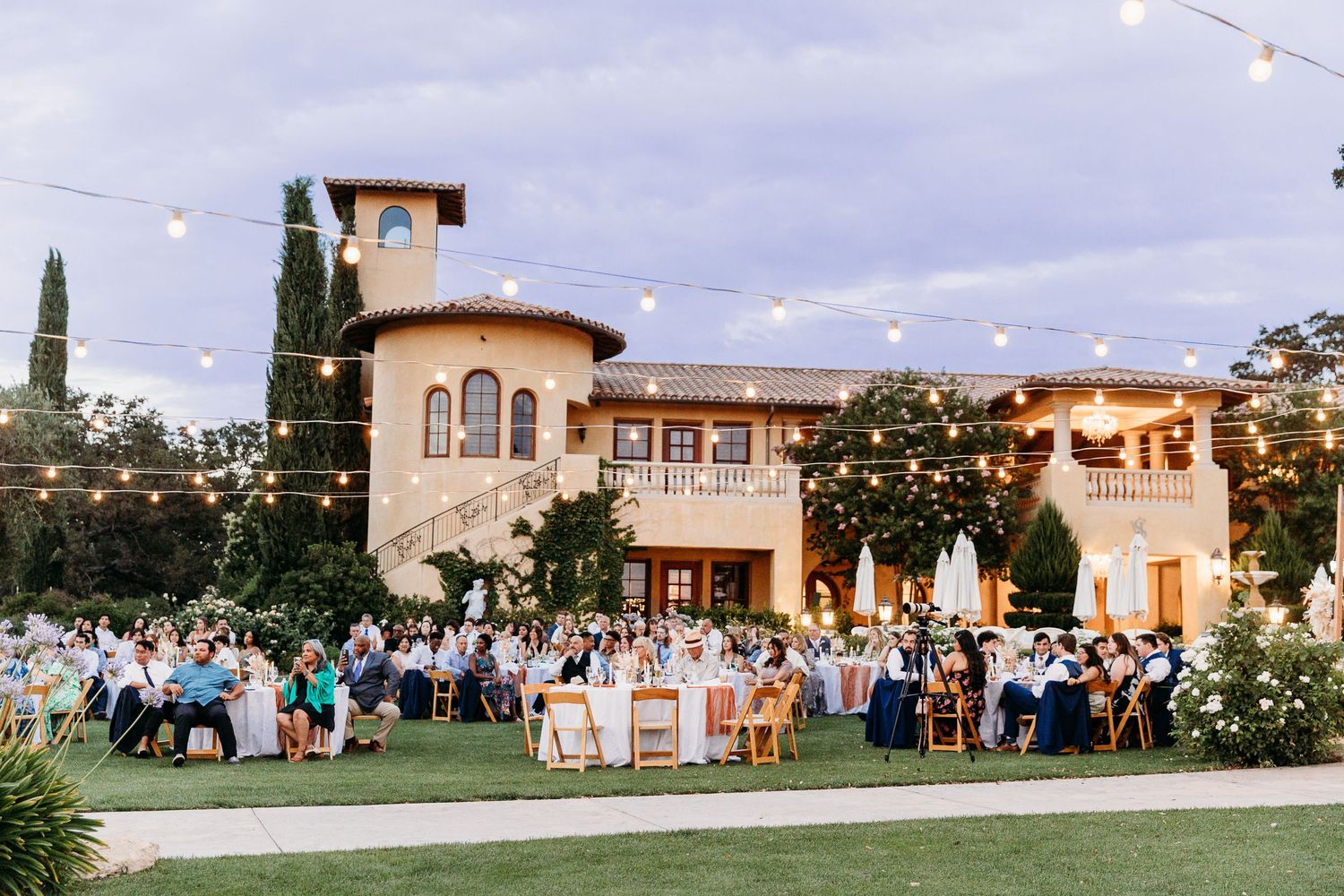 An outdoor wedding reception at a Tuscan-style villa with string lights and dining tables.