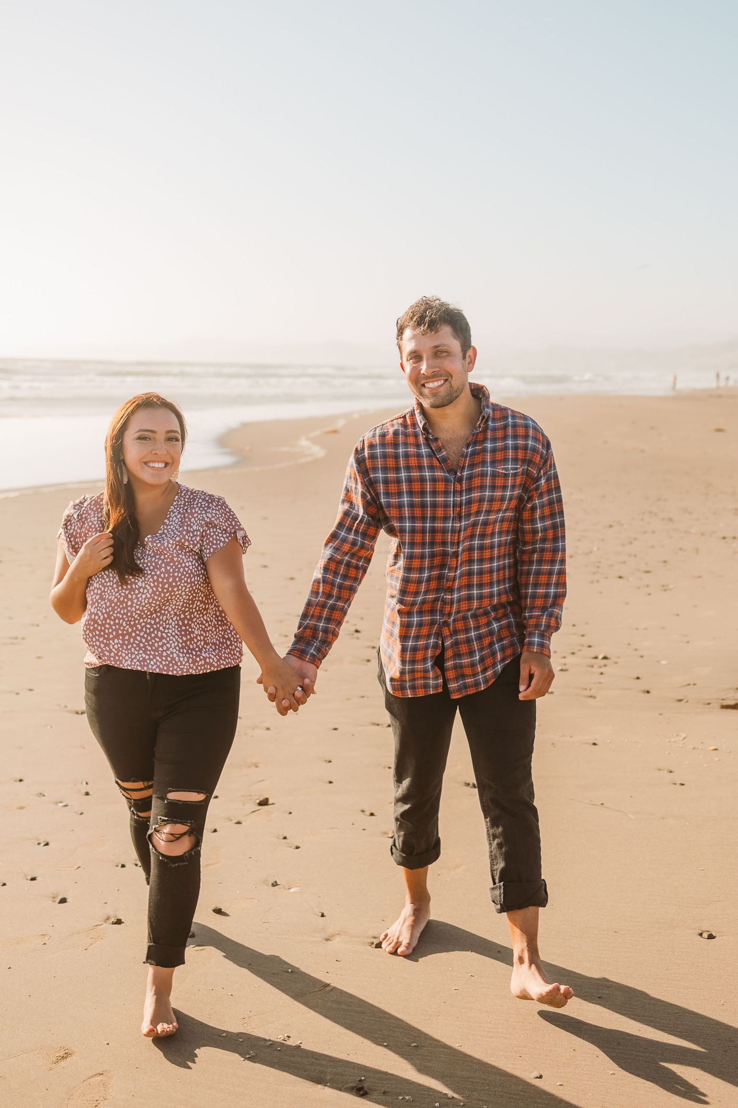 A couple holding hands while walking barefoot together on a sunny beach.