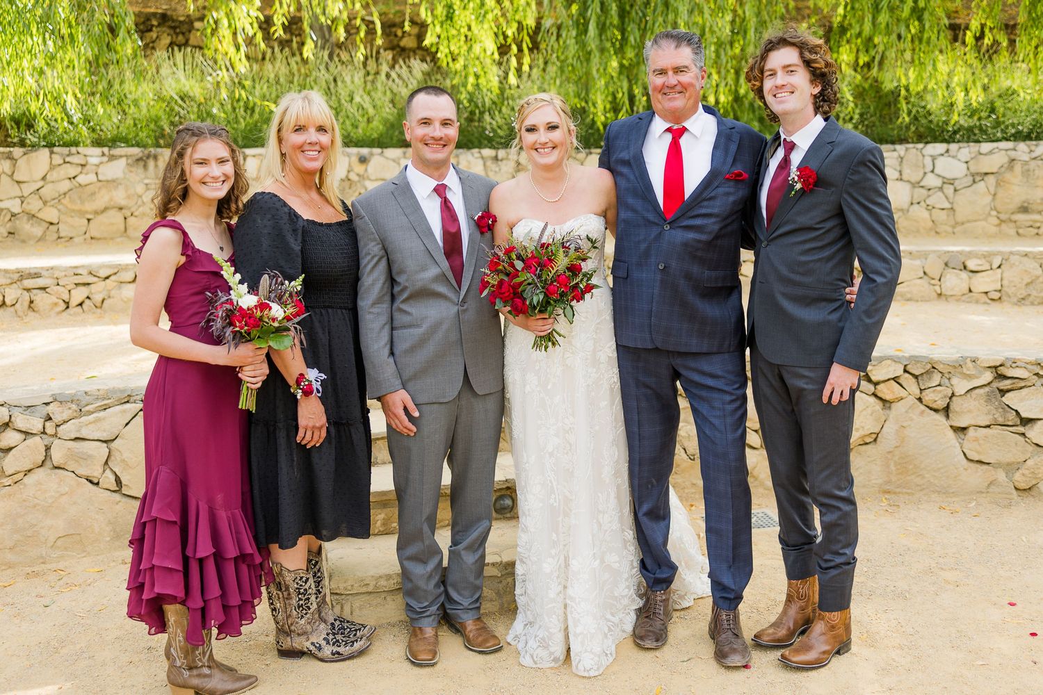 Small wedding group poses on stone steps with burgundy and gray color scheme.