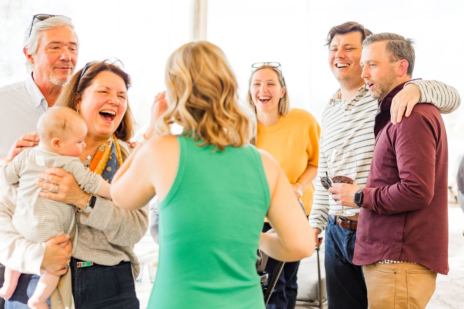 Group of people laughing together during a casual indoor social gathering wearing colorful casual attire.