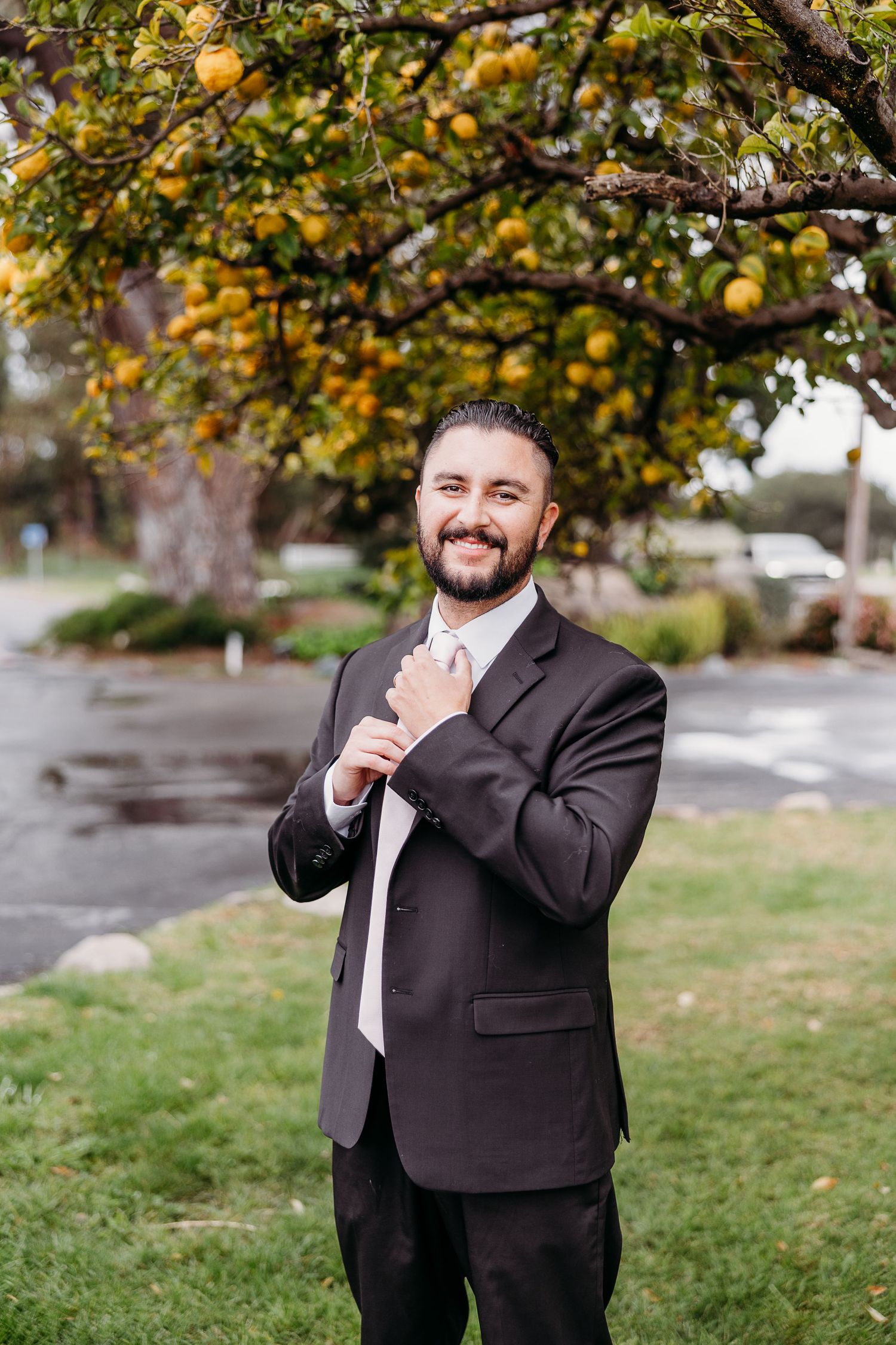 Person in a dark suit laughs joyfully outdoors with autumn trees and yellow leaves in the background.