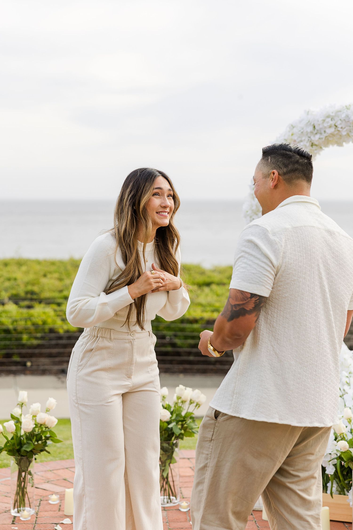 A couple shares a joyful moment during an outdoor celebration with ocean views and floral arrangements.