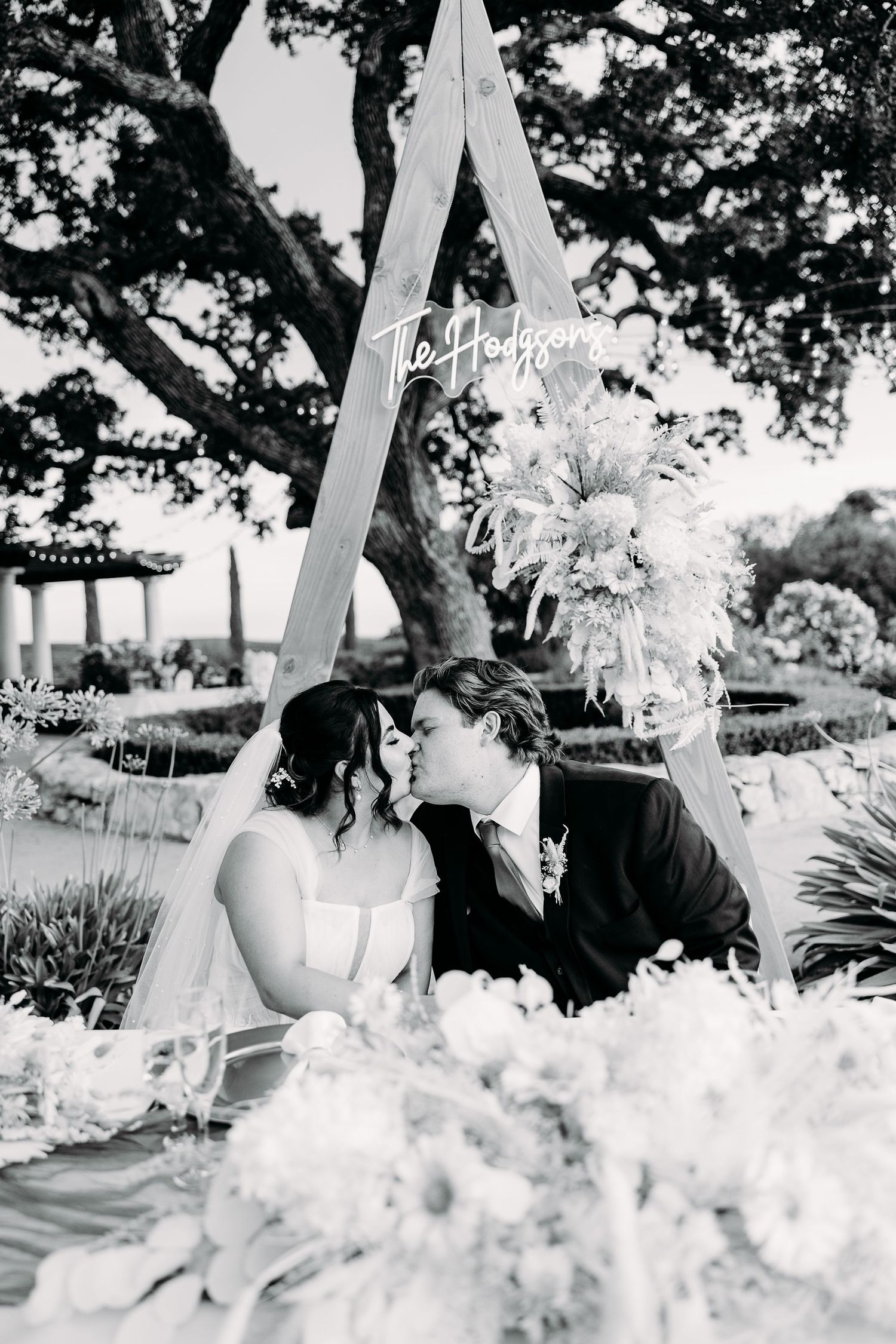 Black and white portrait of wedding couple sharing intimate moment at decorated outdoor reception table.