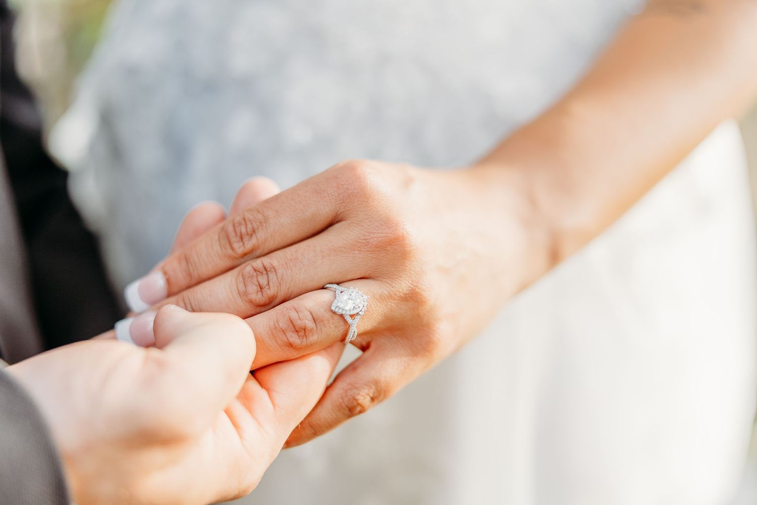 Close-up photo of hands exchanging wedding rings during marriage ceremony against blurred background.