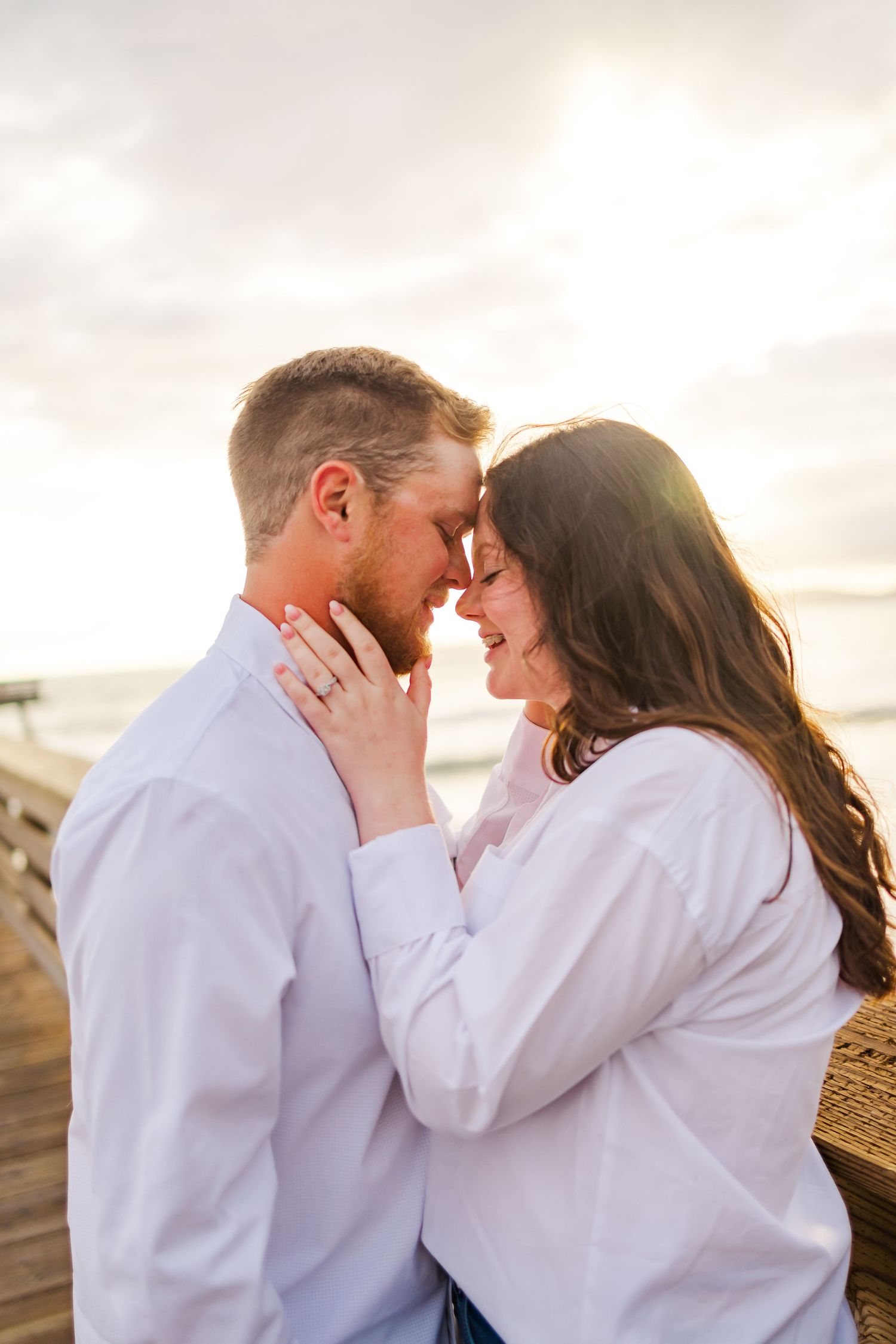 An intimate moment between a couple in white shirts on a seaside pier during sunset.