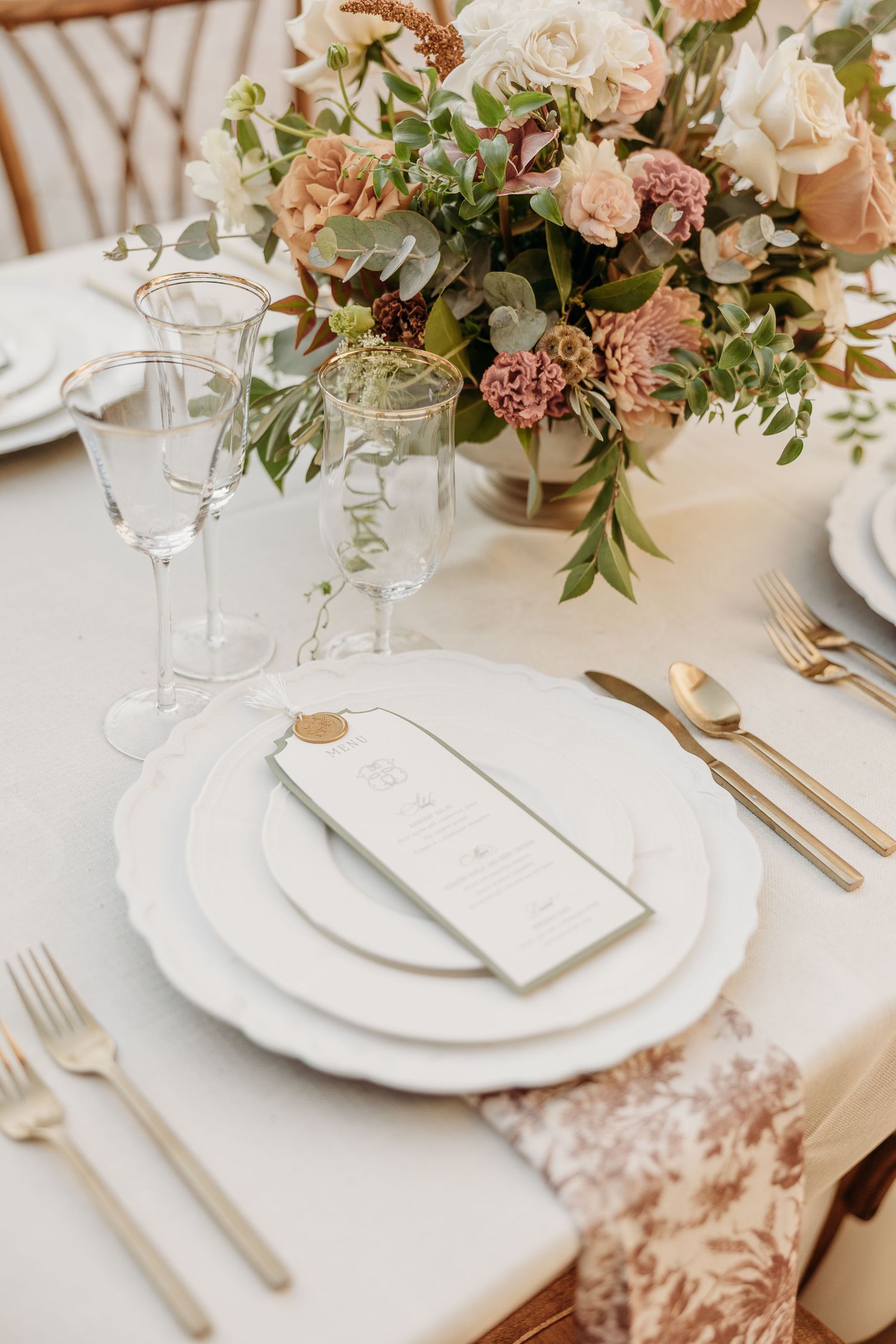 Elegant wedding table setting with white plates, gold cutlery and soft pink floral centerpiece.