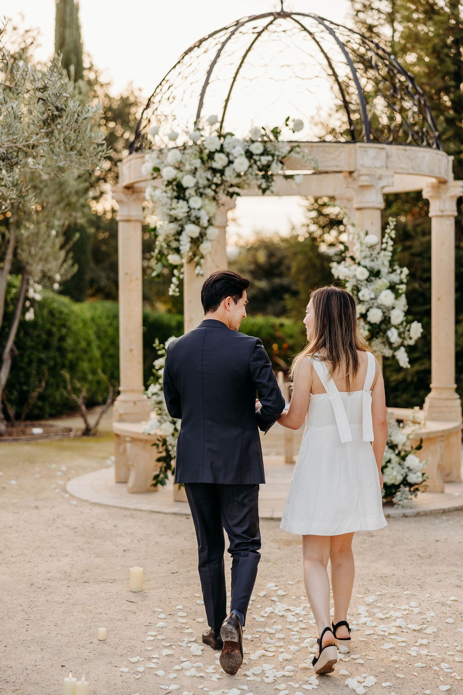 A romantic garden scene with stone gazebo decorated in white floral arrangements.