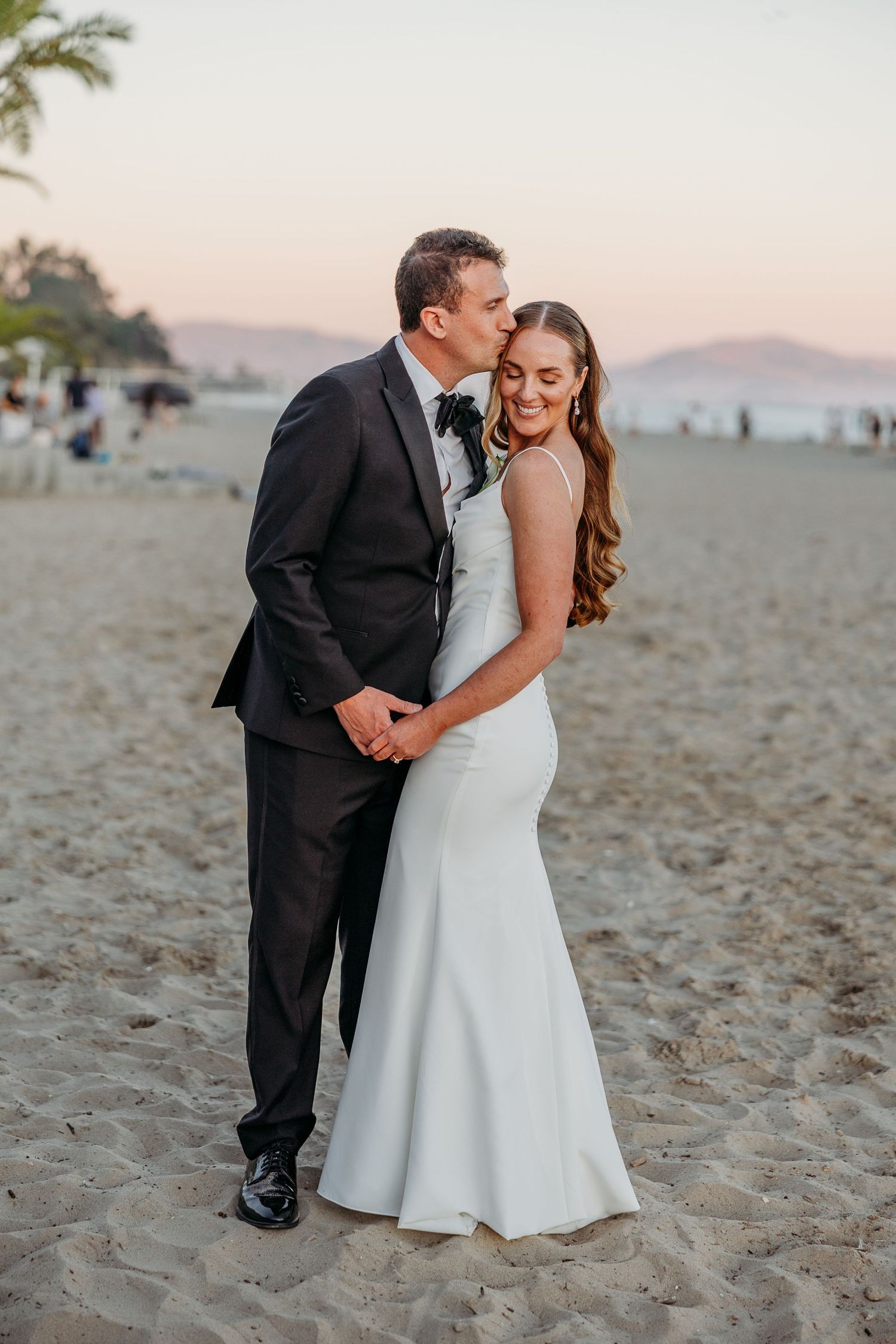 A romantic beach photoshoot at sunset with a couple embracing on sandy shores.