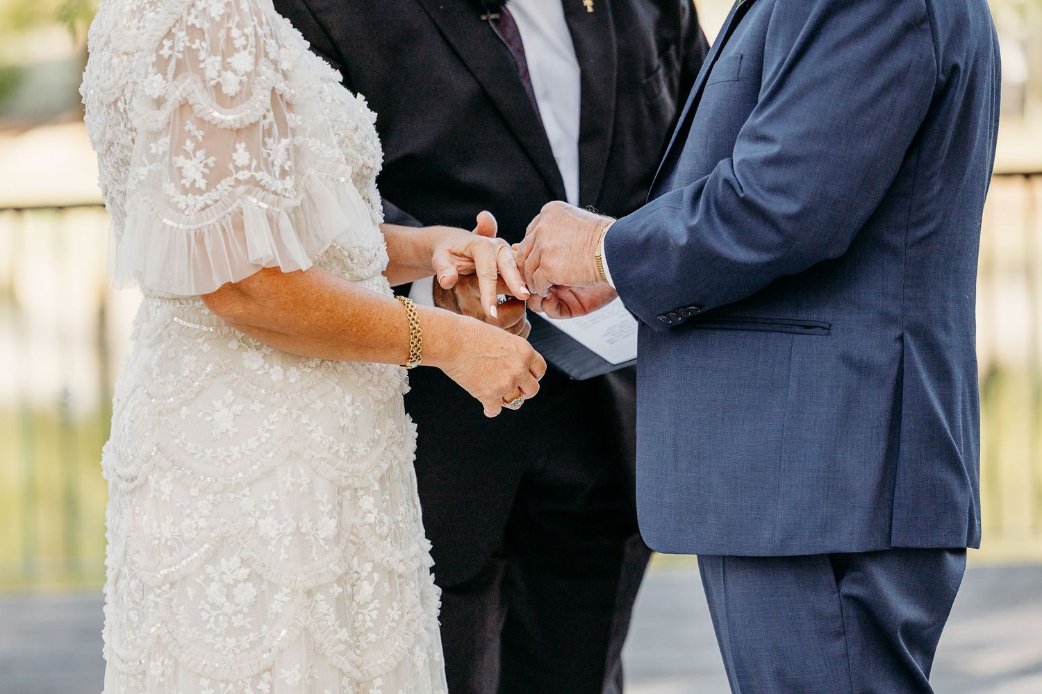 Wedding ceremony close-up showing exchange of rings between couple in formal attire.