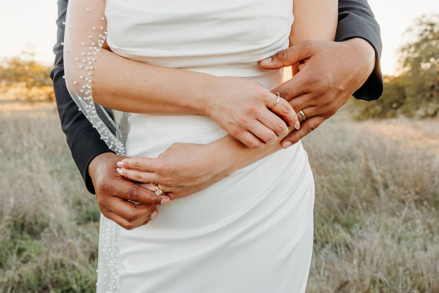 Close-up detail shot of a white wedding dress with hands gently touching the fabric.