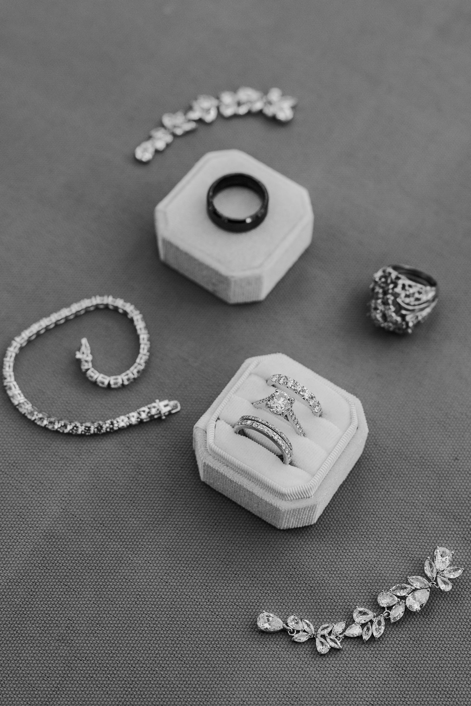 Black and white photo of elegant wedding jewelry including rings, bracelets and necklaces displayed on hexagonal stands.