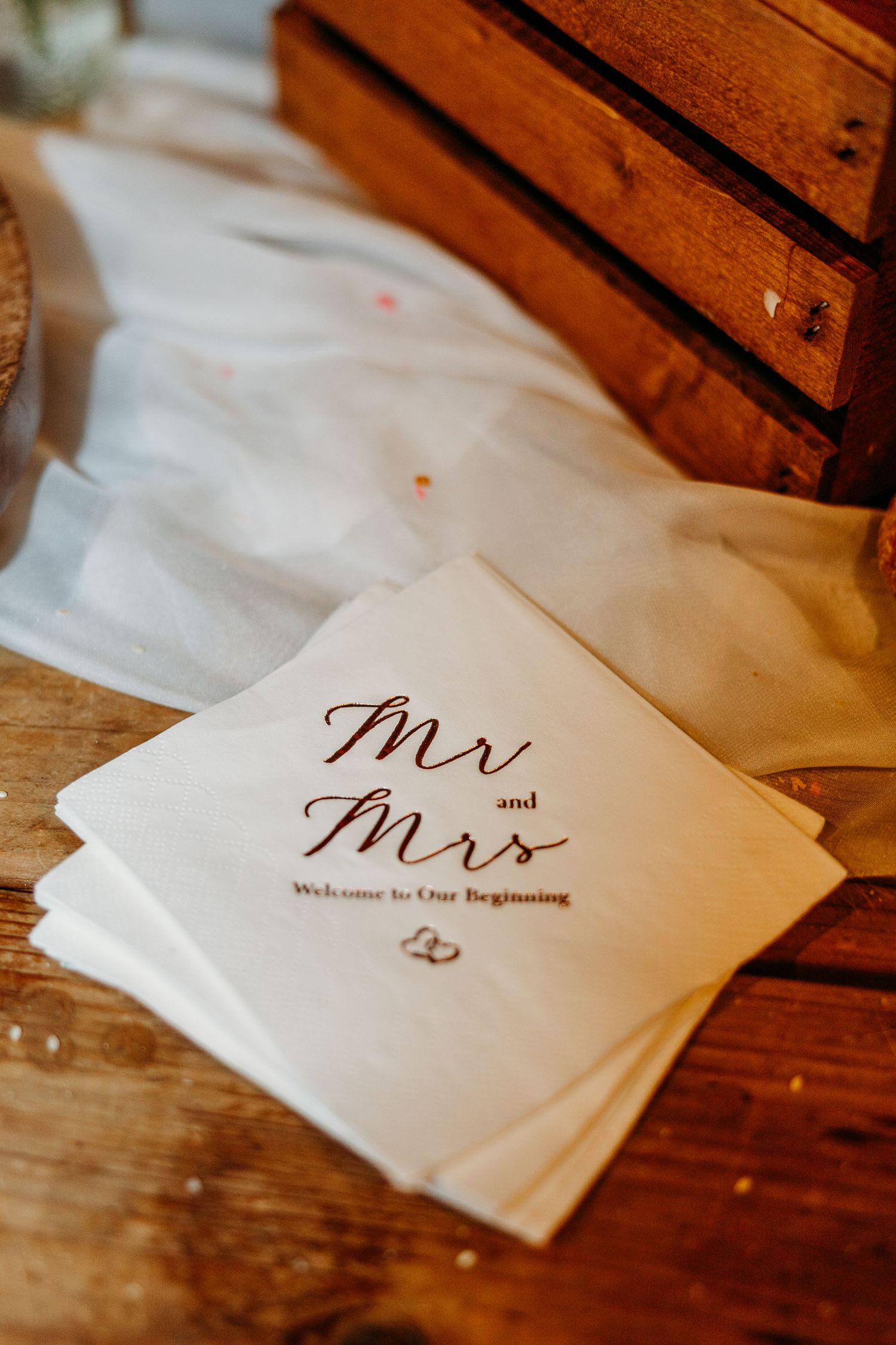 White wedding napkins with 'Mr' and 'Mrs' text arranged on wooden surface with gold rings.