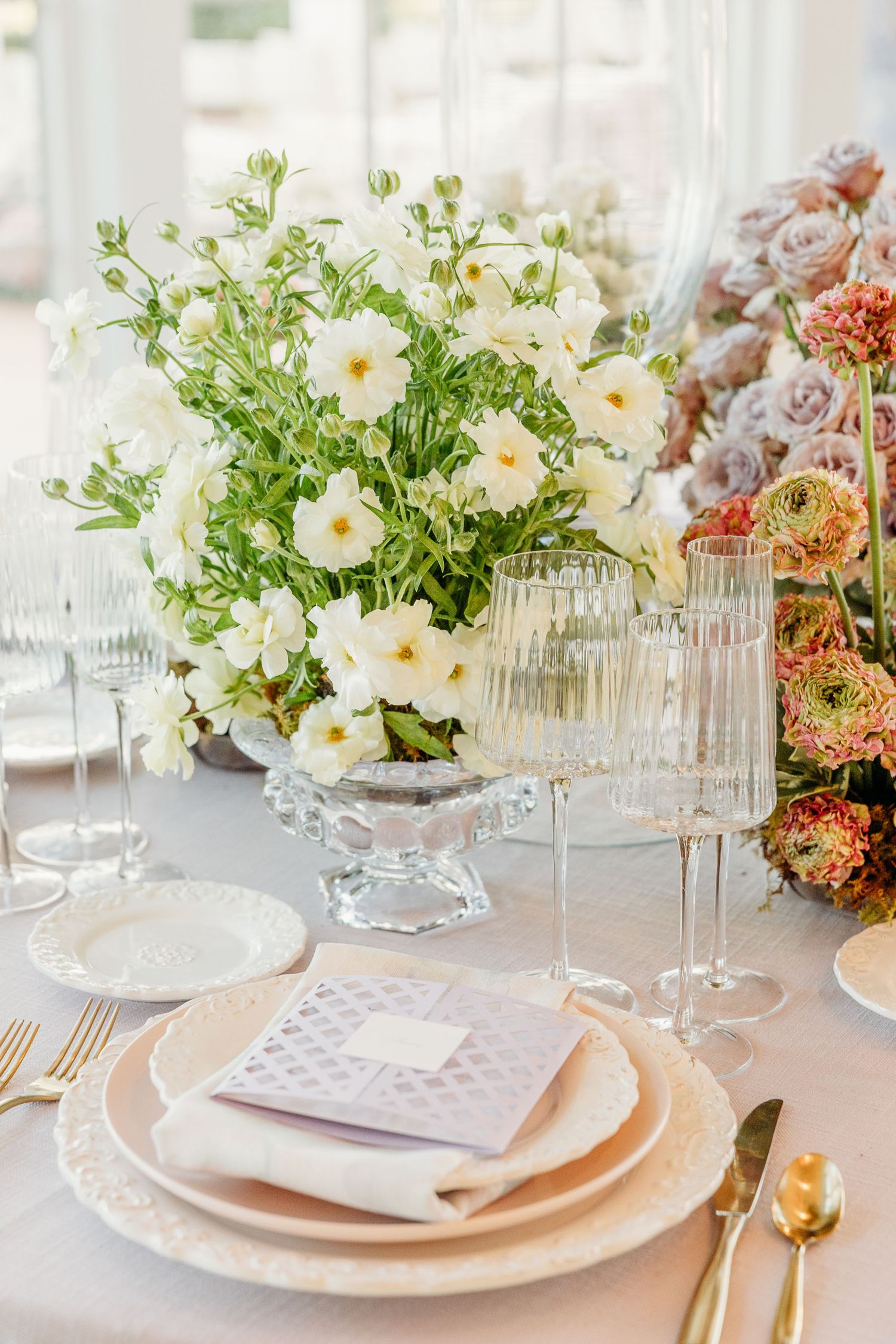 Romantic table setting with crystal glassware, white plates and fresh floral centerpieces in soft pastel colors.