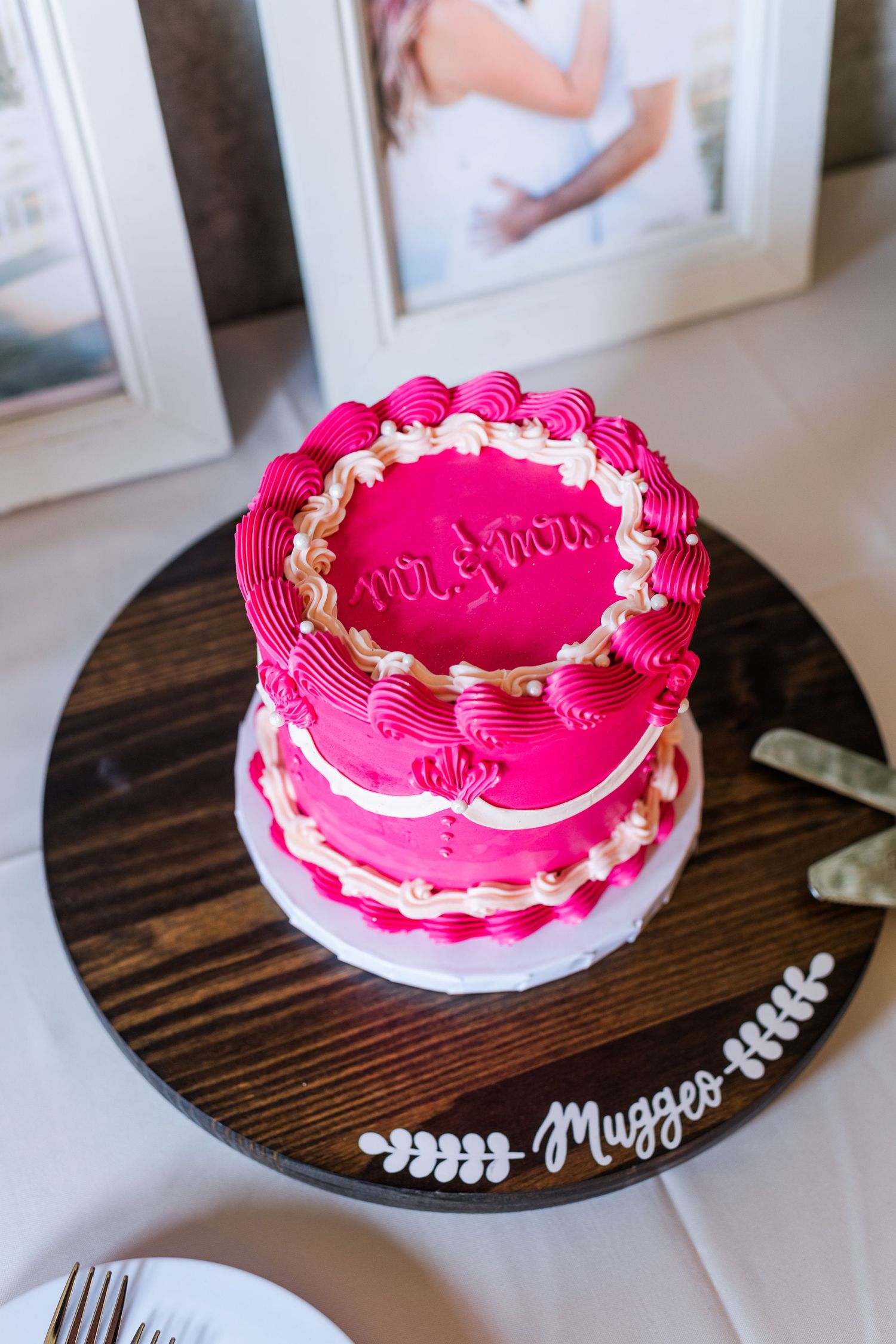 A bright pink celebration cake with white piping sits on a wooden cake stand.