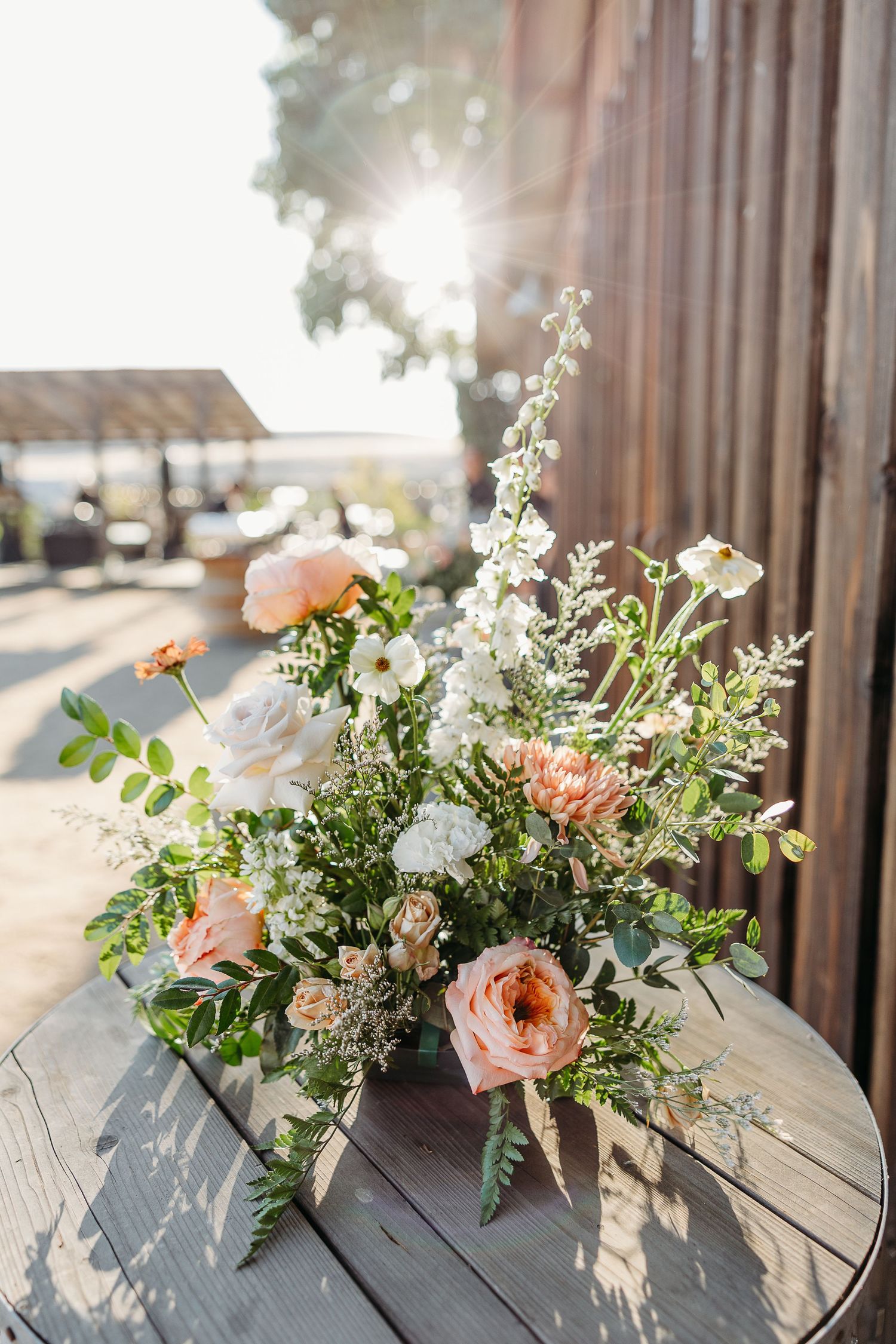 Elegant floral arrangements with peach and white blooms displayed on weathered wood in natural sunlight.