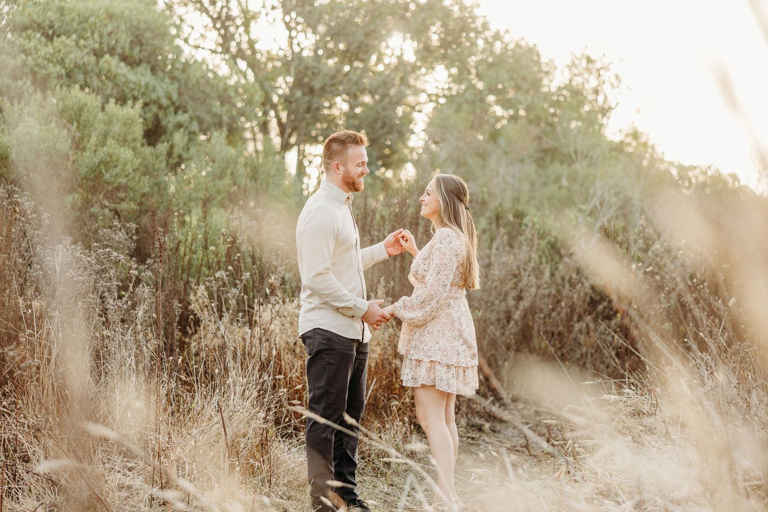 Couple poses together in tall grass during sunset engagement session.