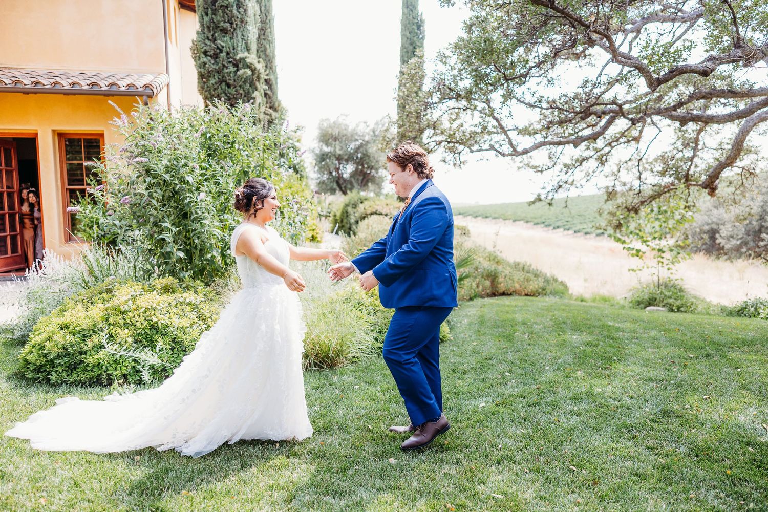 A couple shares a joyful moment dancing on a grassy hill during their wedding day.
