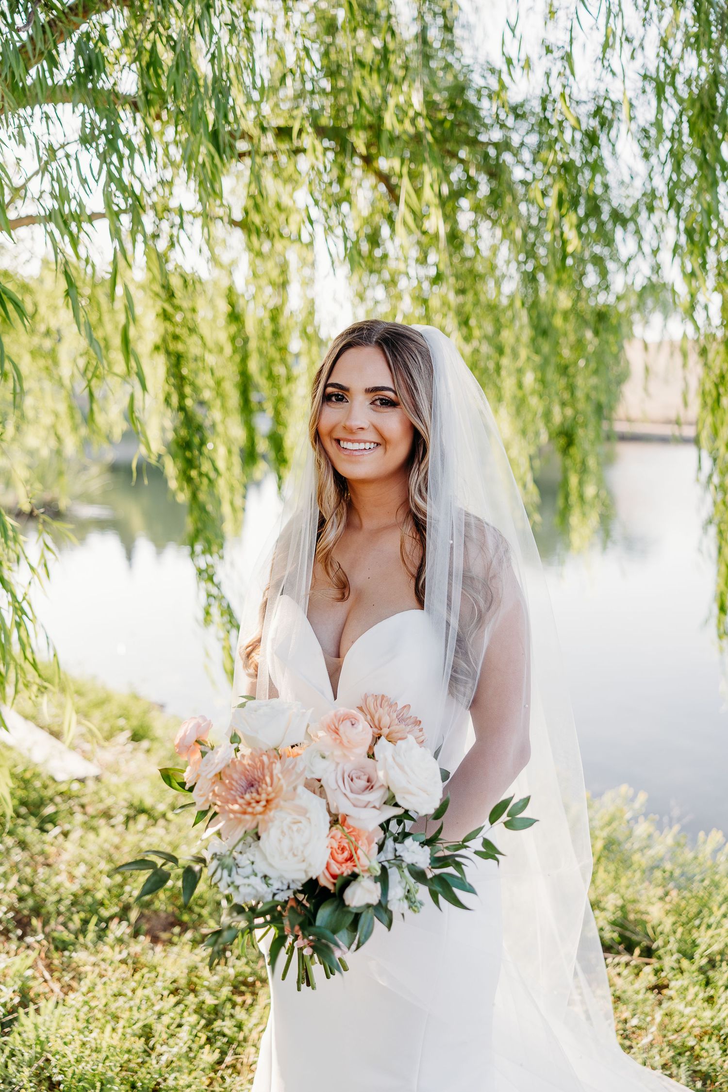 A stunning bridal portrait captured under weeping willow branches beside a serene lake.