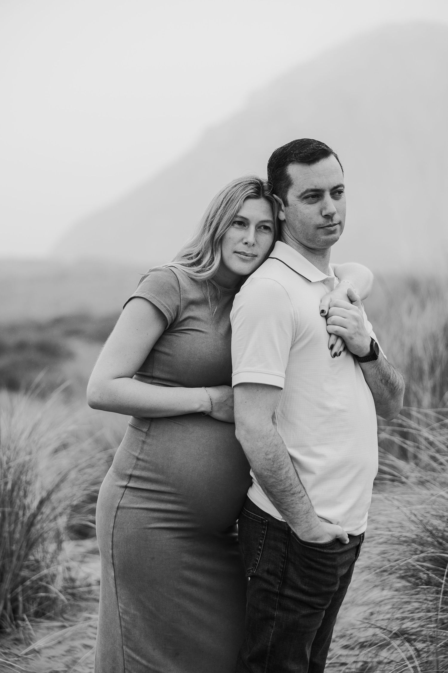 Black and white maternity portrait of couple standing together in natural setting.