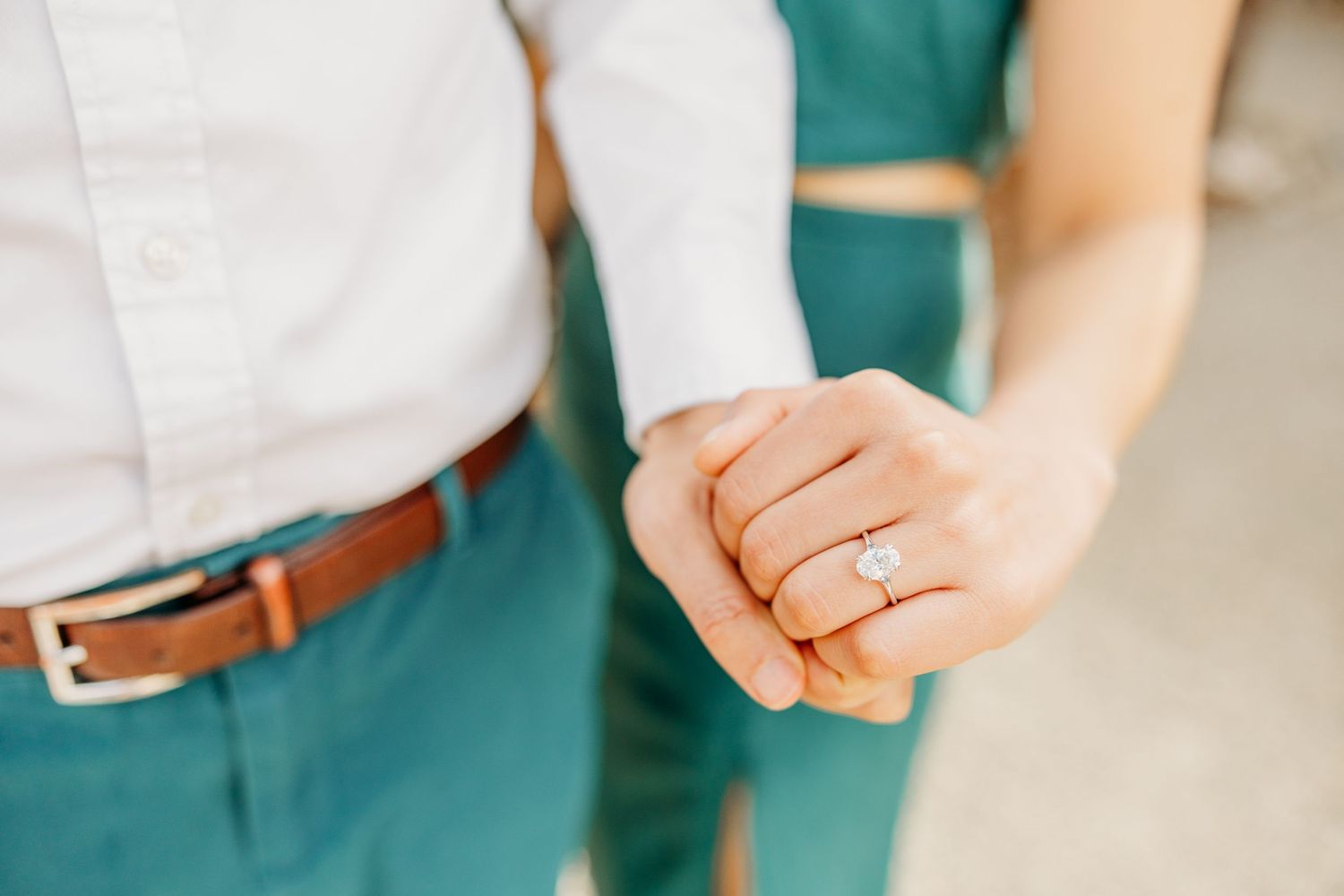 Close-up of joined hands showing an engagement ring against green and white clothing.